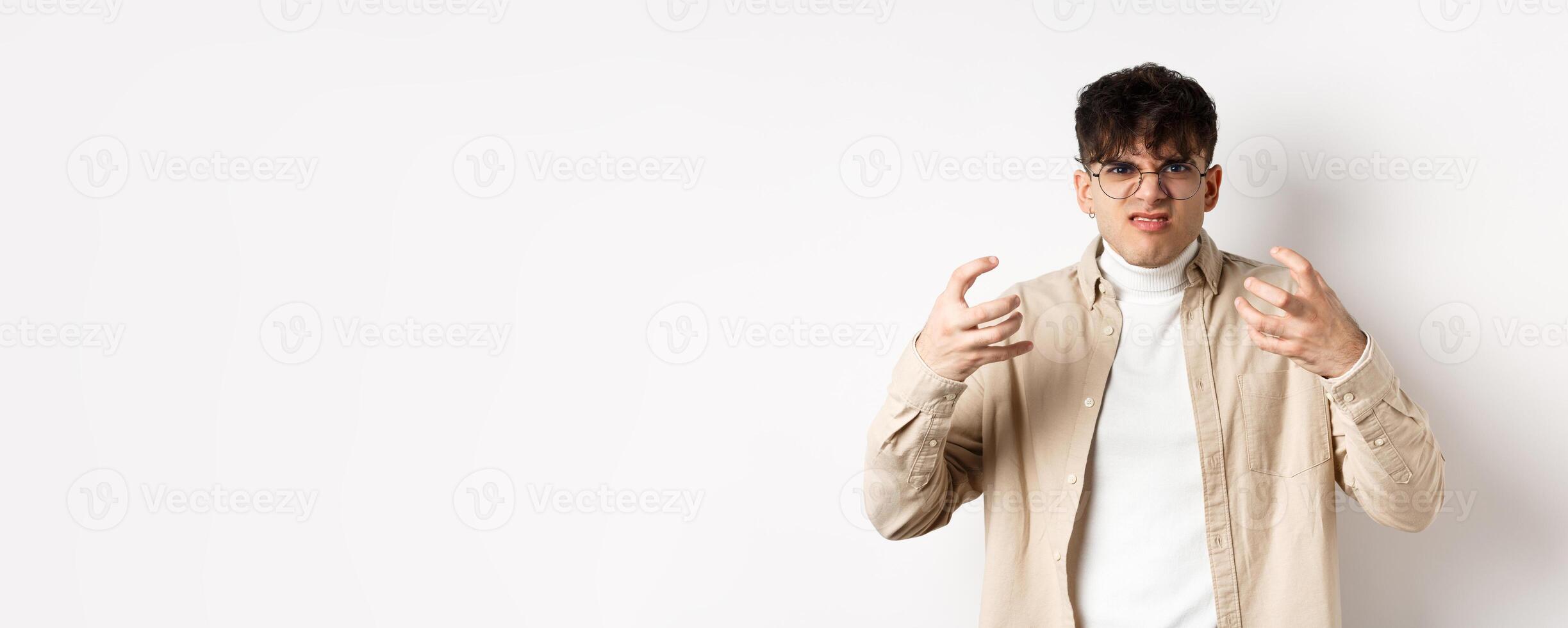 Portrait of annoyed and mad guy wants to strangle someone, grimacing from hatred and clench arms, standing bothered on white background photo