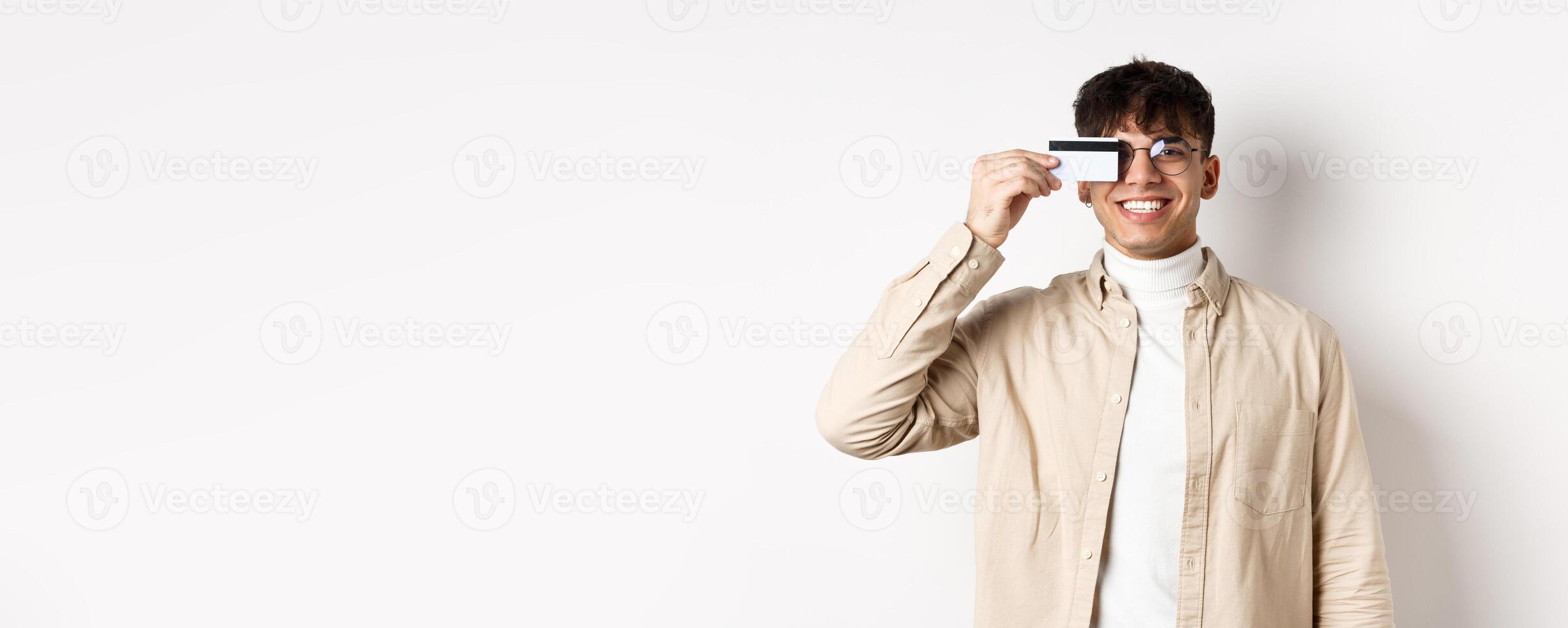 Cheerful young guy smiling real and showing plastic credit card, standing happy on white background, wearing glasses photo