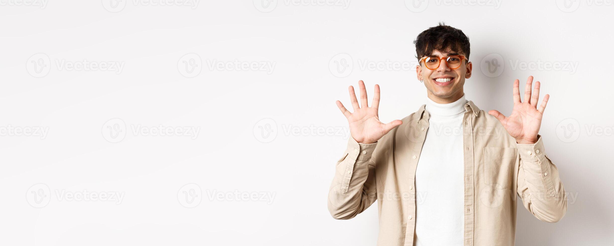 Modern guy in glasses and stylish outfit, showing ten fingers number and smiling, standing on white background photo