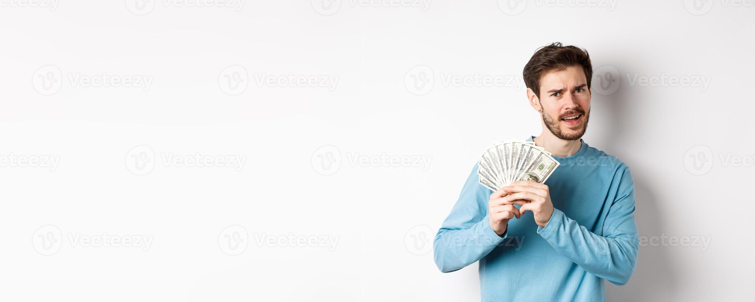 Handsome young man showing money and looking pleased. Guy dancing with dollars, earn income, standing over white background photo