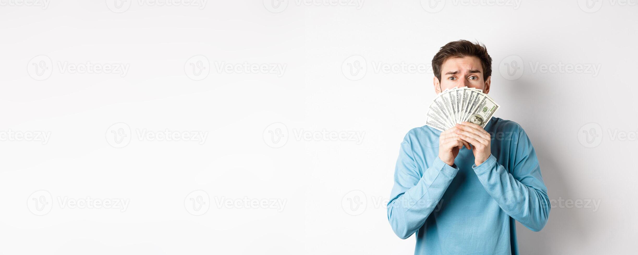 Worried young man looking with pleading face, showing money, standing in blue sweatshirt over white background photo