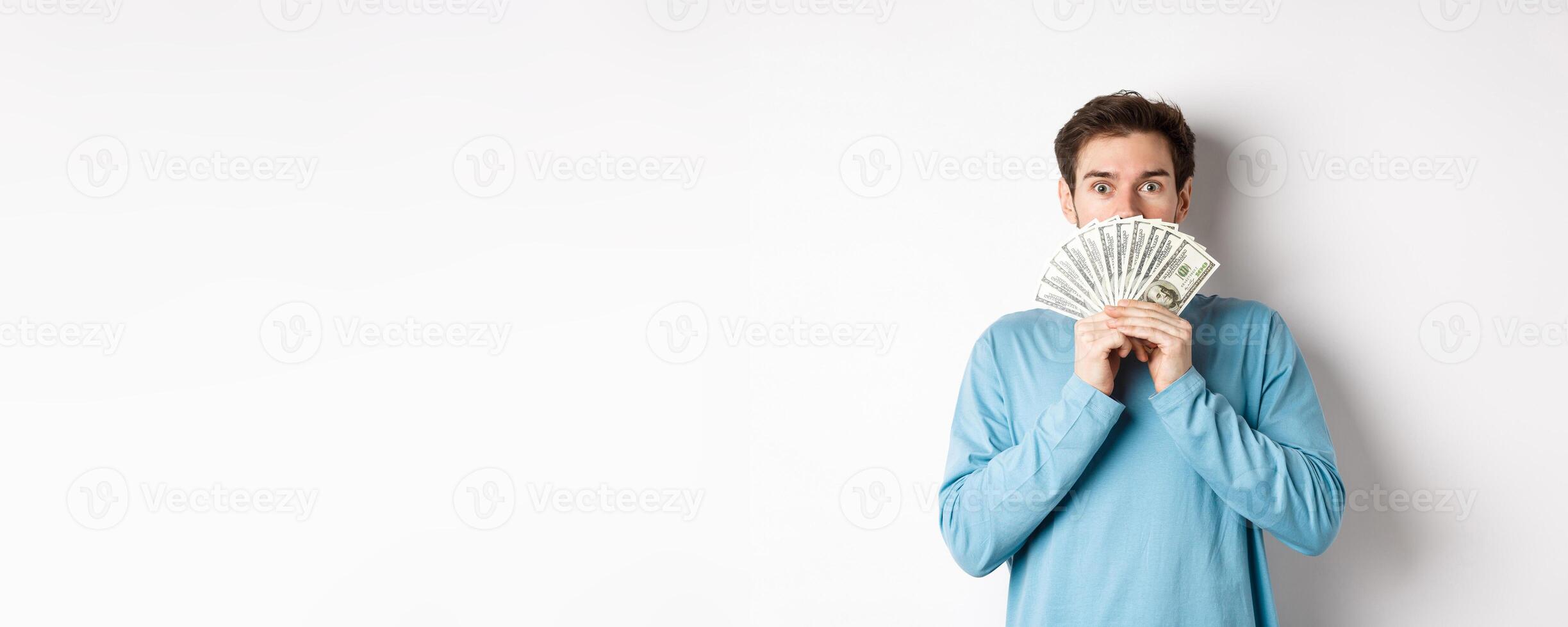 Surprised and amazed handsome guy showing money, looking at promo offer, going shopping with cash, standing over white background photo