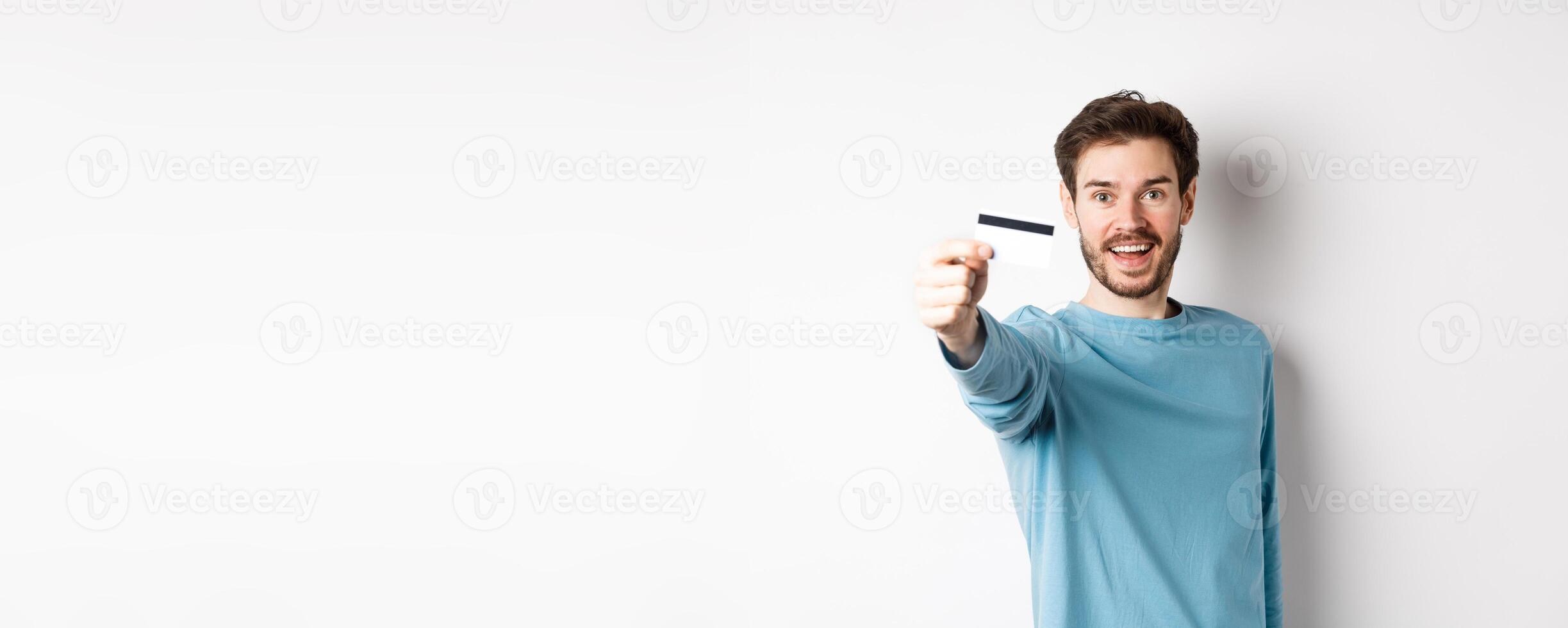 Happy man showing plastic credit card and smiling, recommending bank, standing over white background photo
