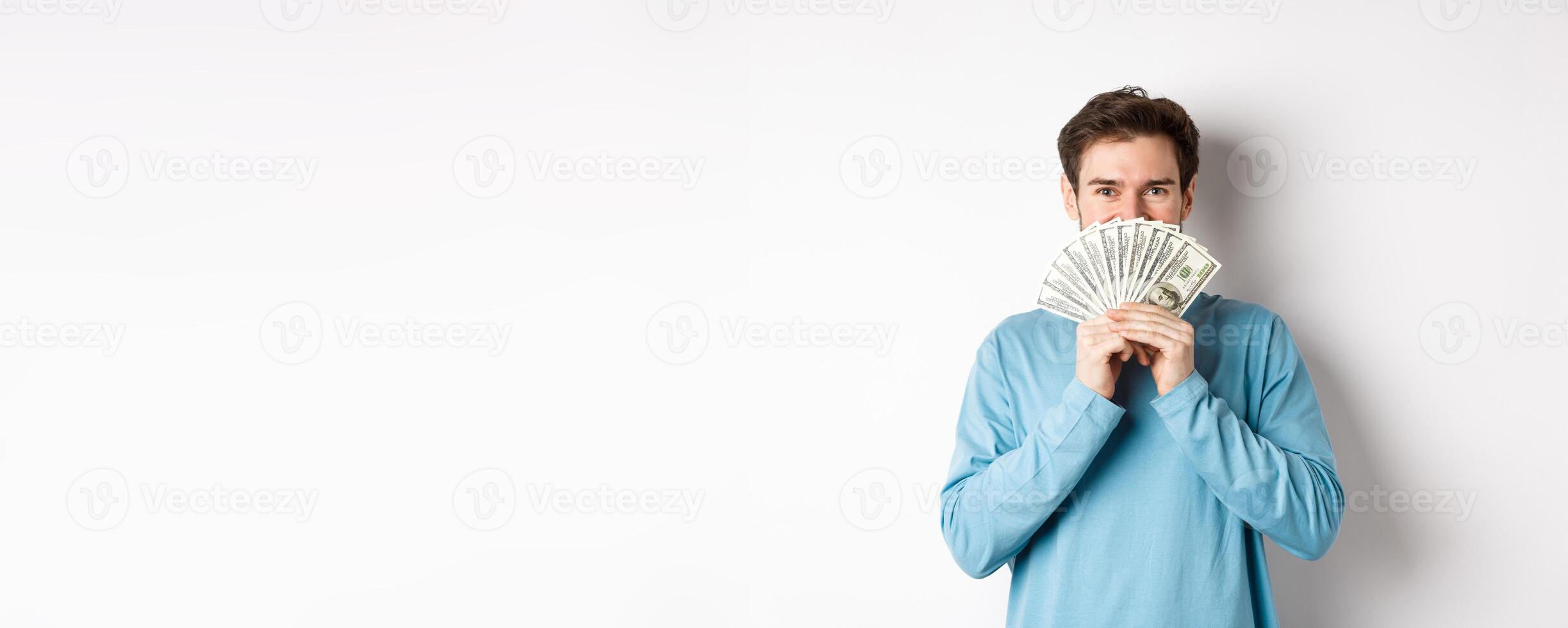 Cheerful shopper holding money for shopping, standing with dollars and smiling, standing over white background in casual clothes photo