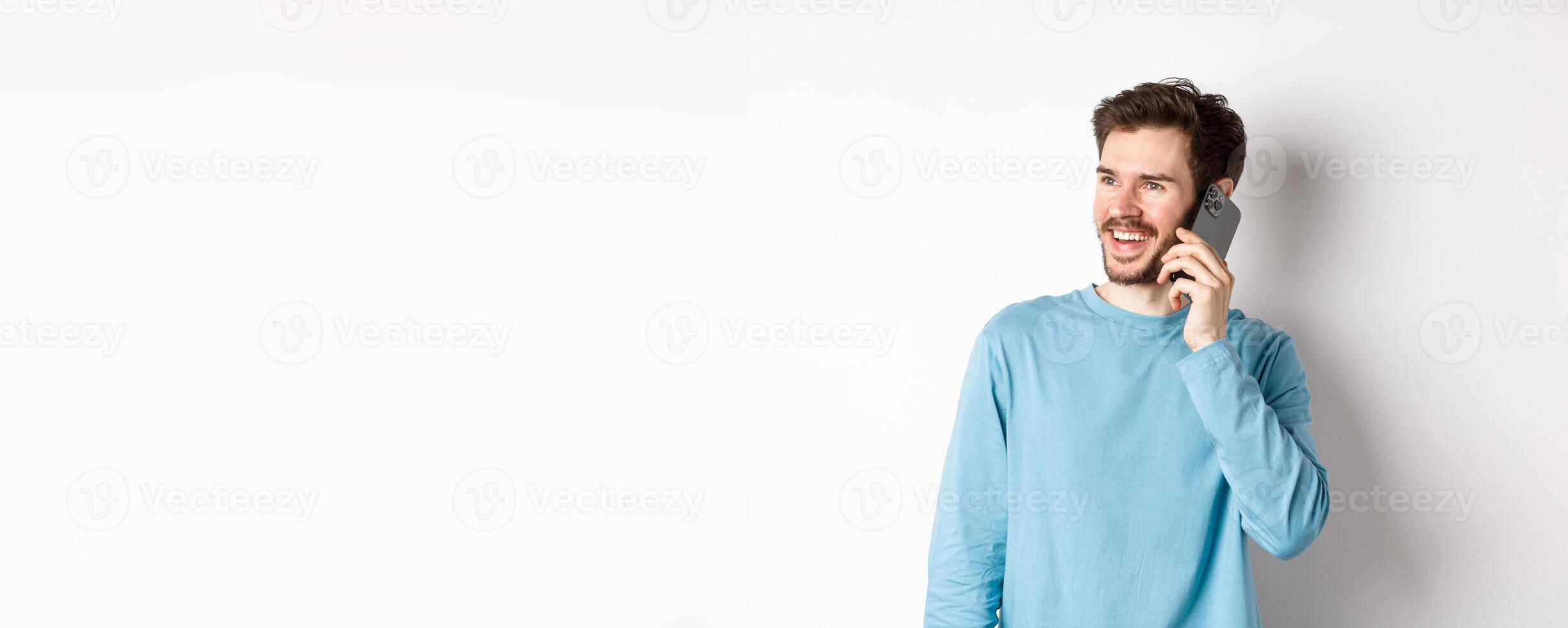 Technology concept. Joyful man enjoying phone call, talking on smartphone and smiling, standing in casual shirt over white background photo