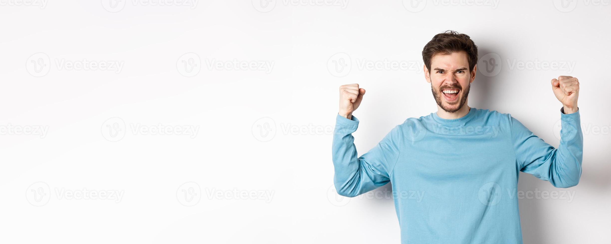 Portrait of satisfied handsome man winning prize, rejoicing in triumph, celebrating victory and shouting yes, standing over white background photo