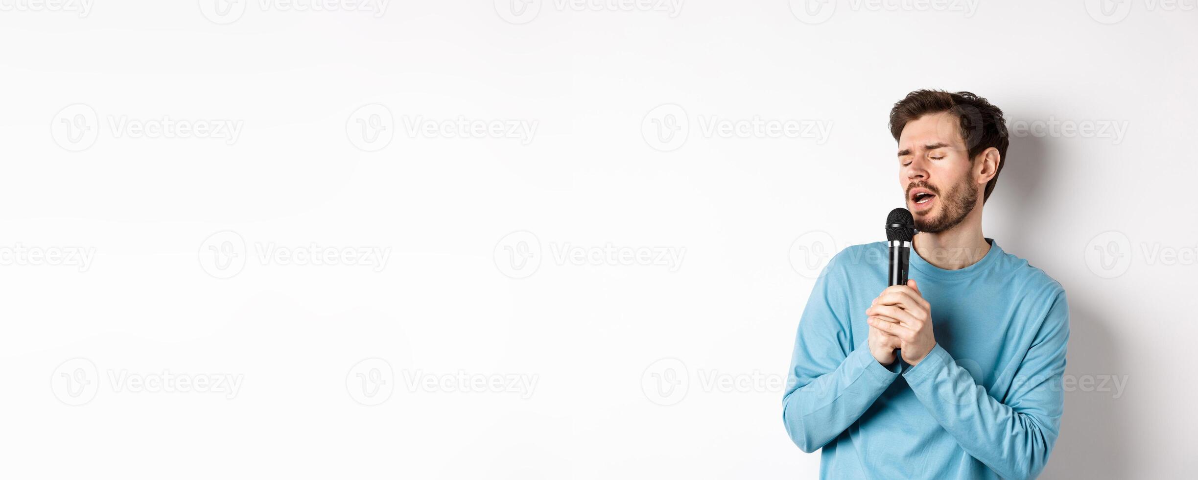 Young caucasian man singing song in microphone with carefree face, standing in karaoke over white background photo