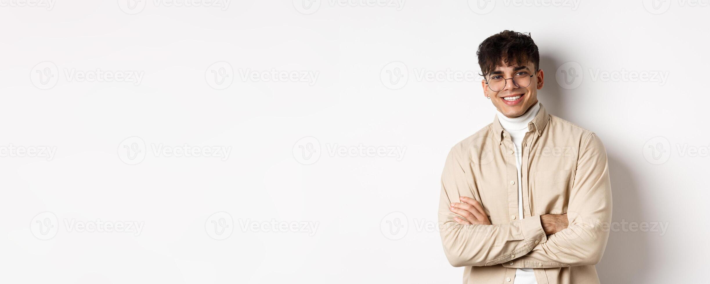 Handsome young man in glasses cross arms on chest, smiling at camera carefree, standing on white background photo