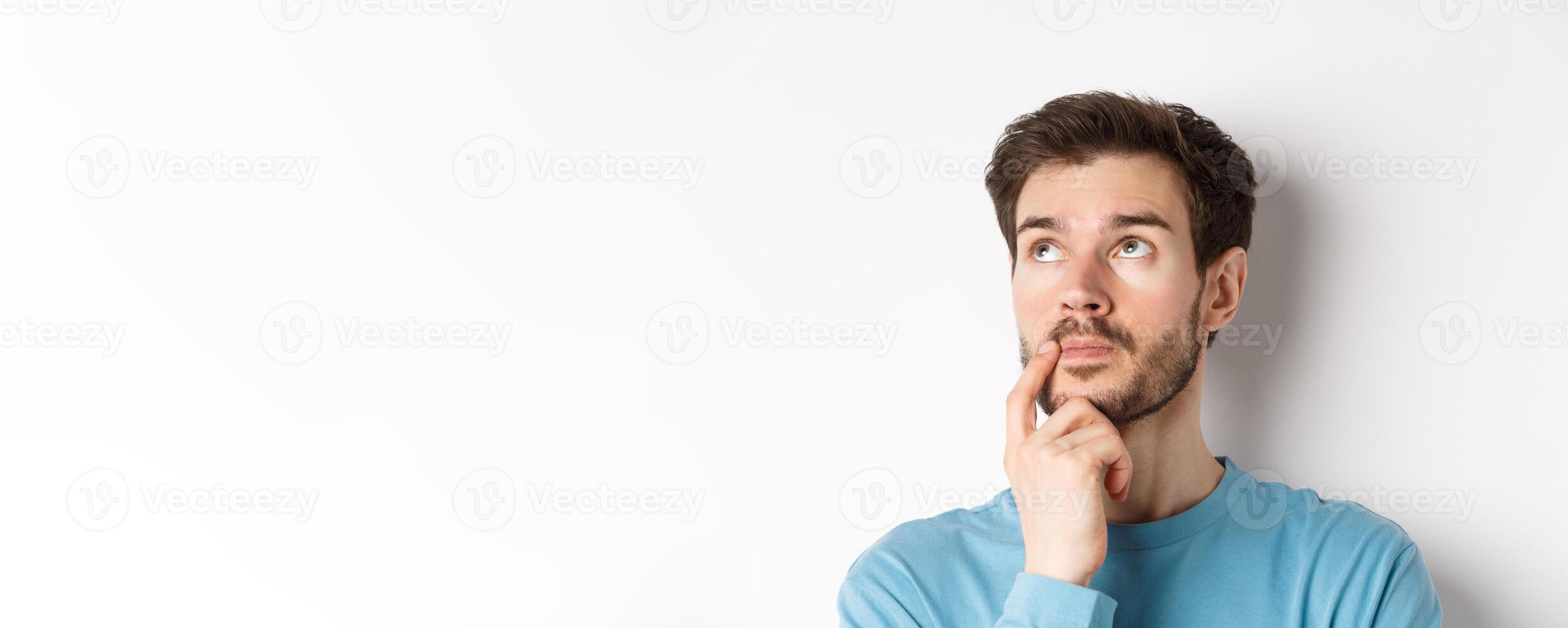 Face of young caucasian man looking up pensive, making choice or thinking, pondering while standing over white background photo