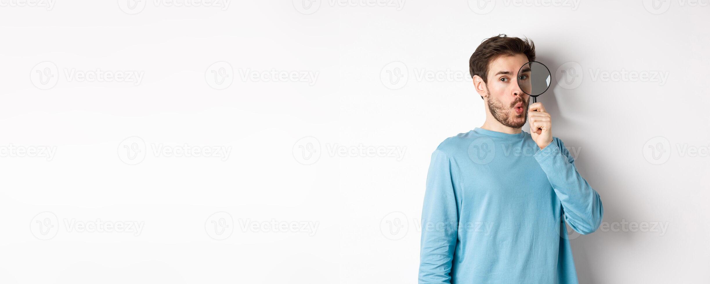 Surprised man found something, looking through magnifying glass with amazed face, standing over white background photo