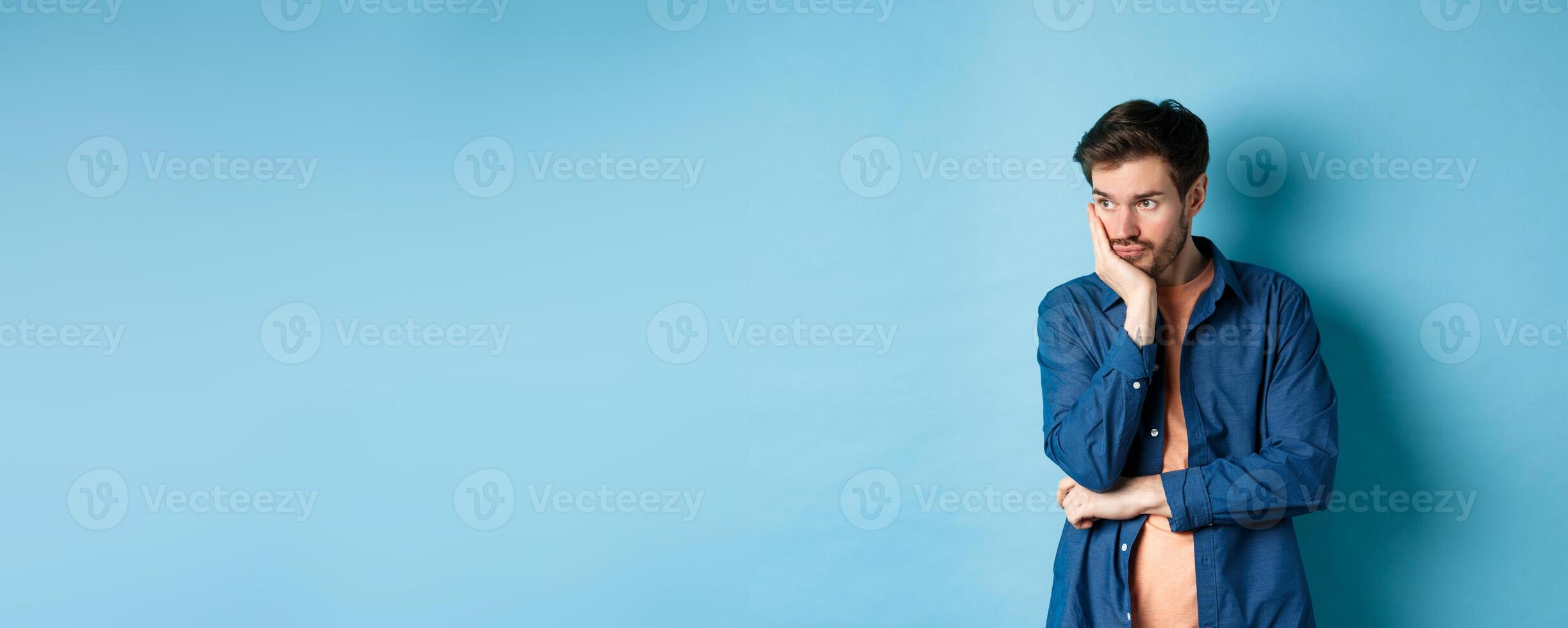 Tired and bored man space out, looking away with empty head, staring at something aside, standing on blue background photo
