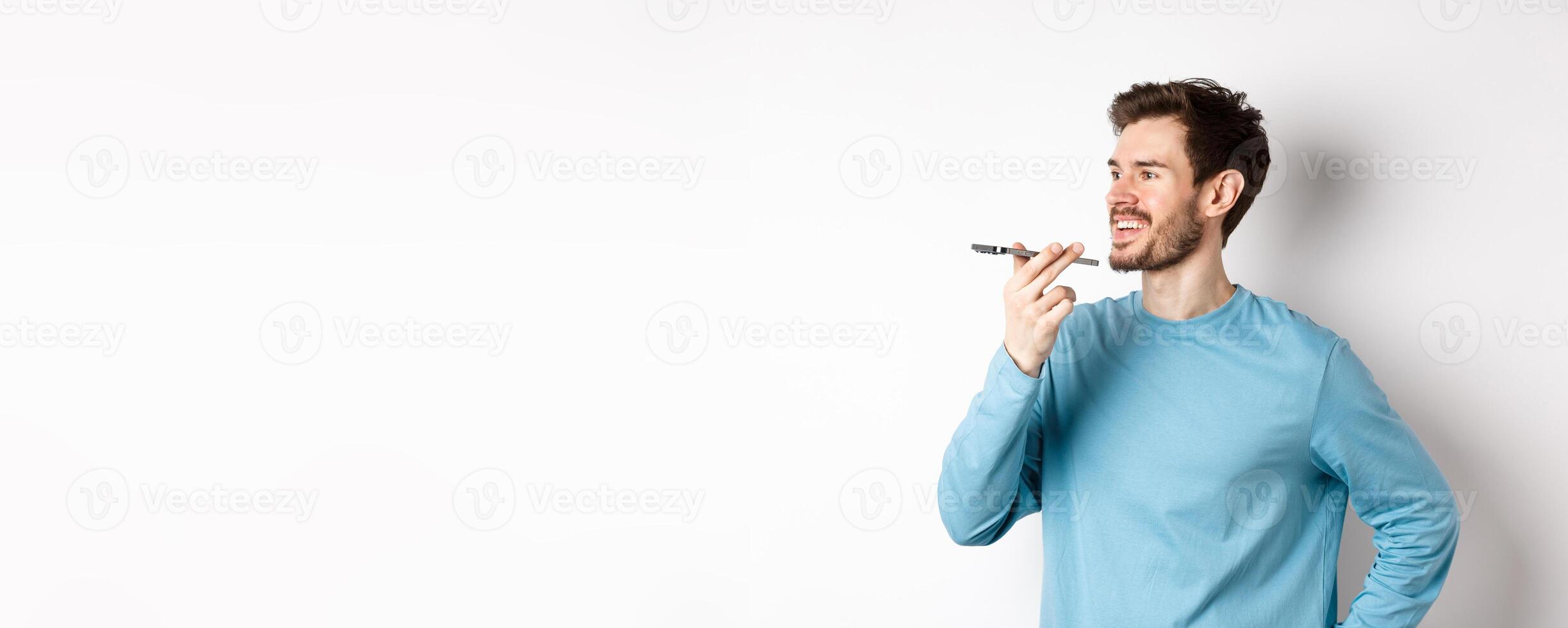 Young man talking on speakerphone or translating voice recording on application, standing happy on white background photo