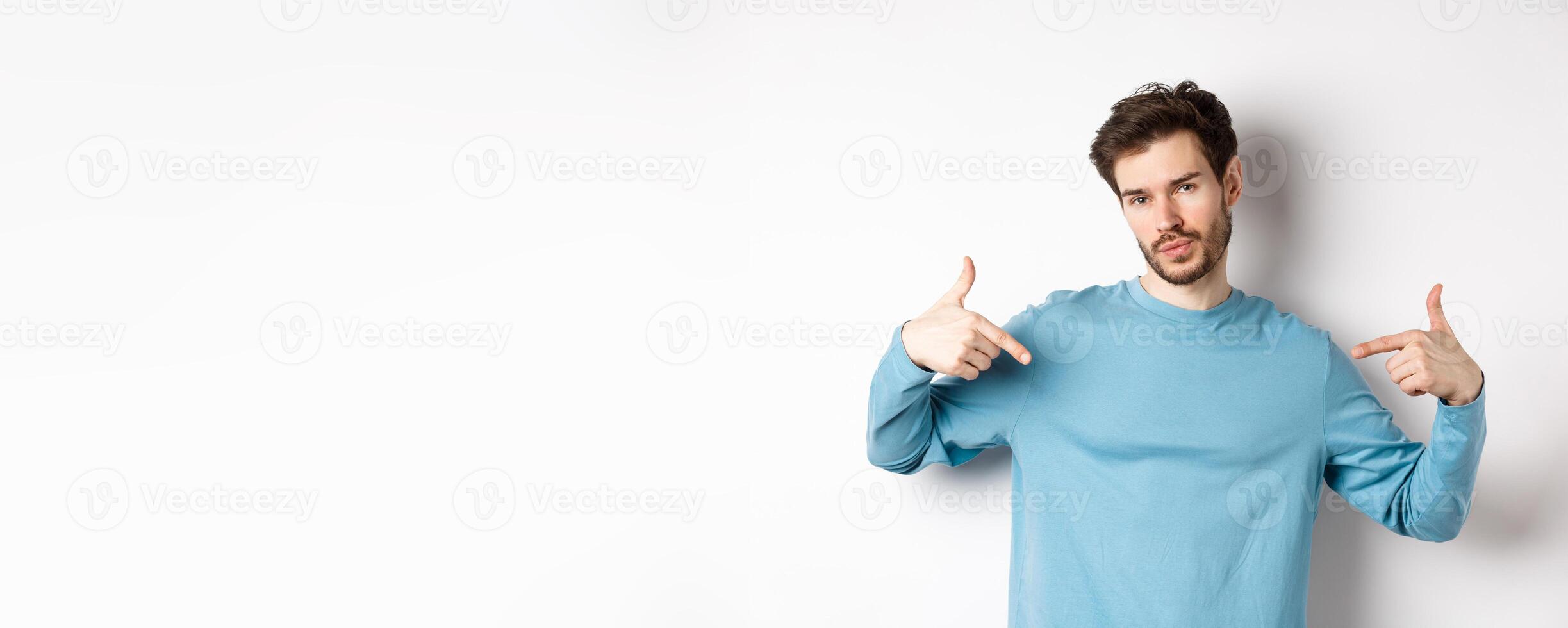 Young man with beard feeling confident, pointing at himself and making smug face, standing on white background cool and sassy photo