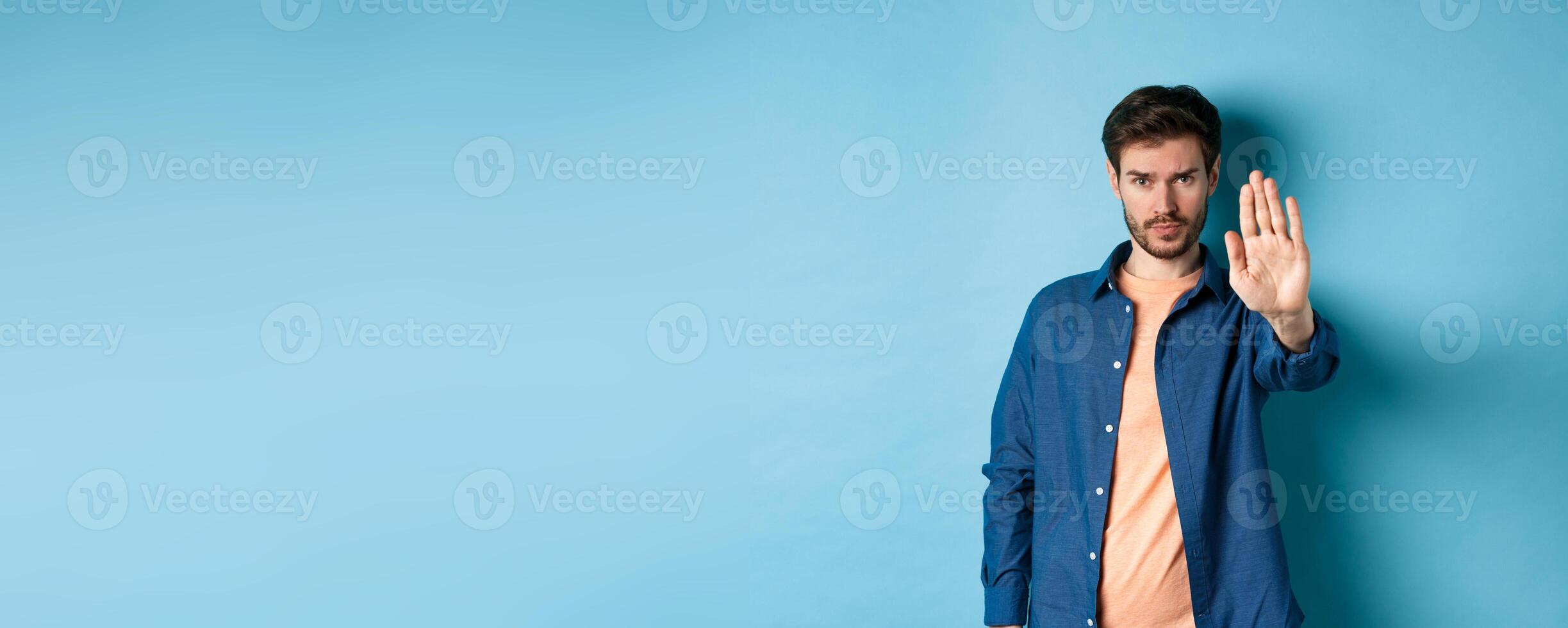 Upset man frowning and asking to stop, stretch out hand to prohibit or disagree with something bad, standing on blue background photo