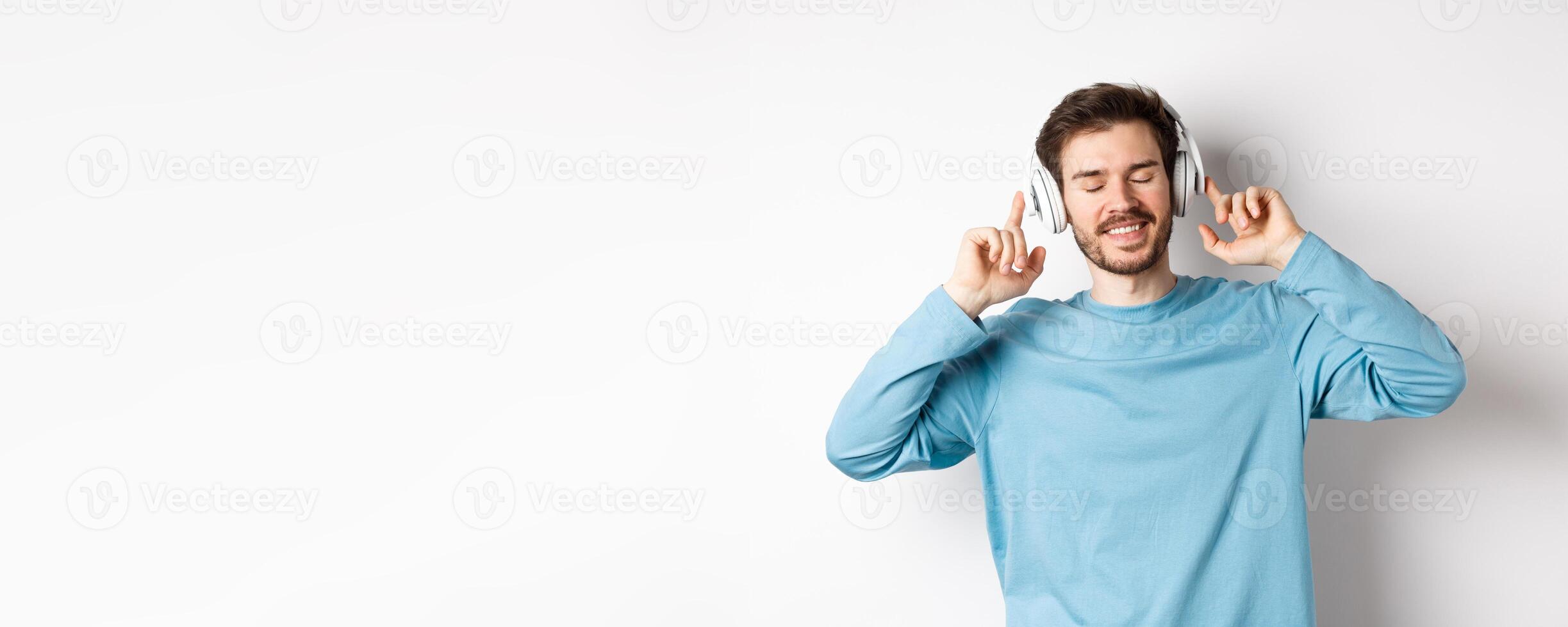 Handsome man listening music in wireless headphones and smiling, enjoying good sound, white background photo