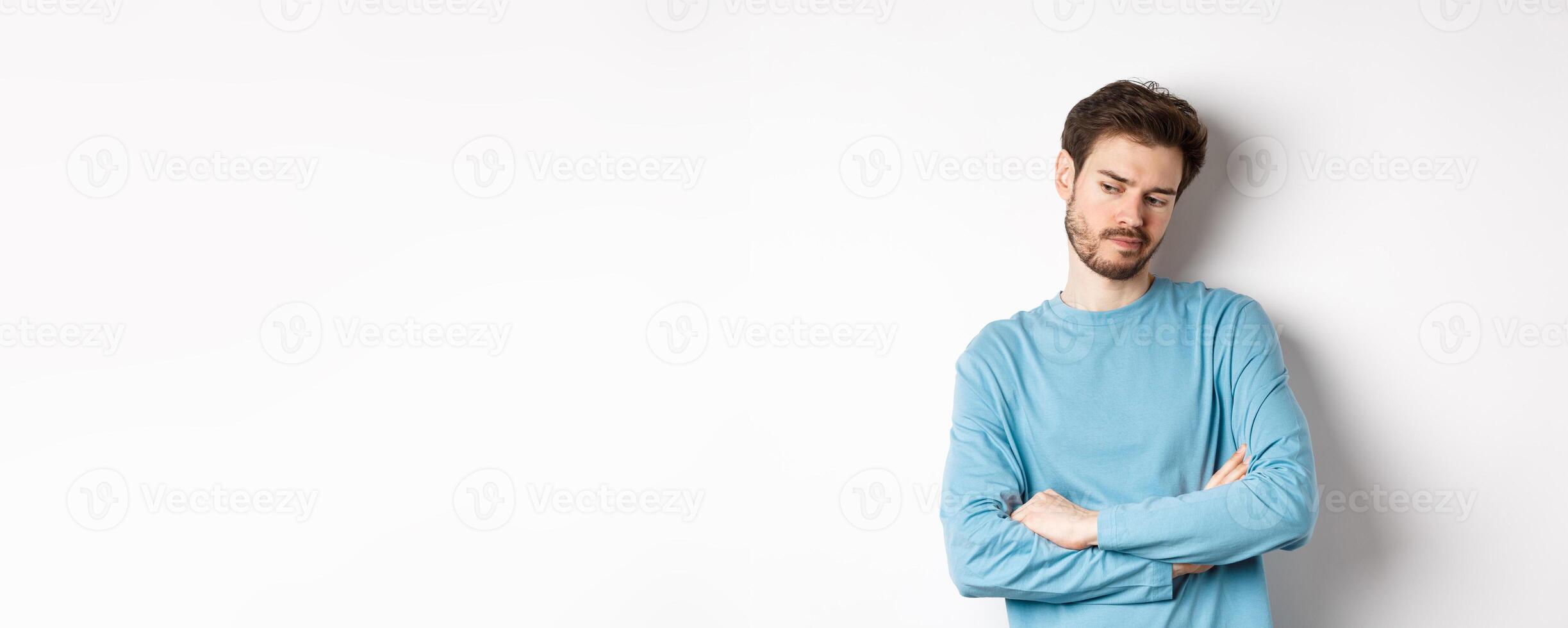 Indecisive and thoughtful bearded man thinking, looking down pensive and making choice, standing over white background photo