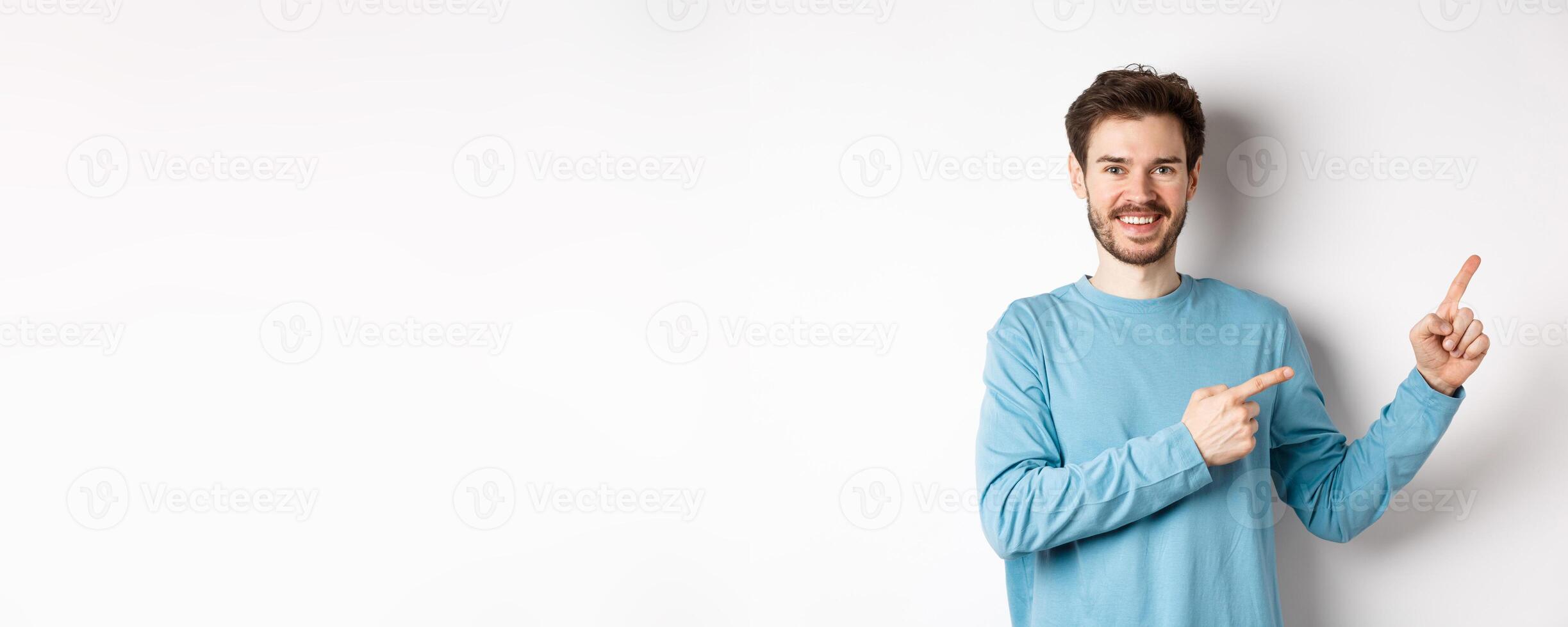 Happy bearded man showing advertisement, pointing fingers right and smiling, inviting to click link, standing over white background photo