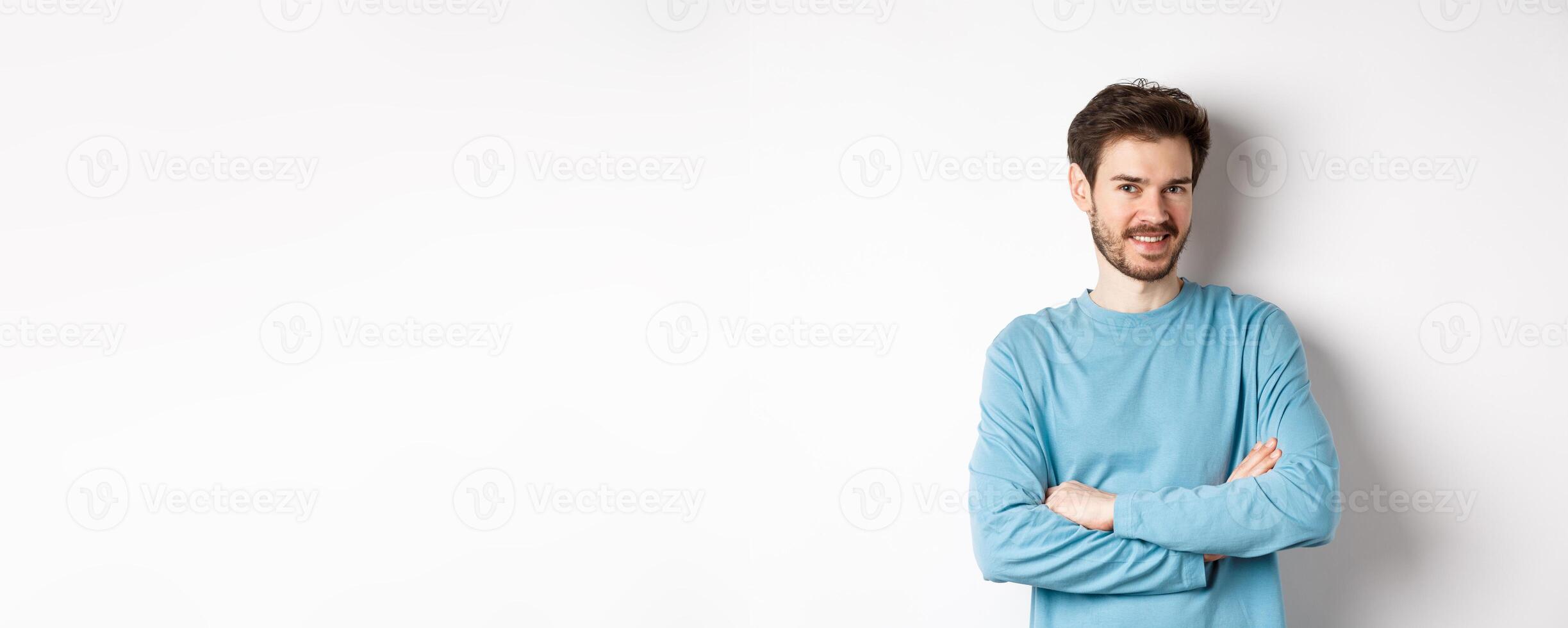 Confident young man with beard, cross arms on chest and smile at camera, standing like professional over white background photo
