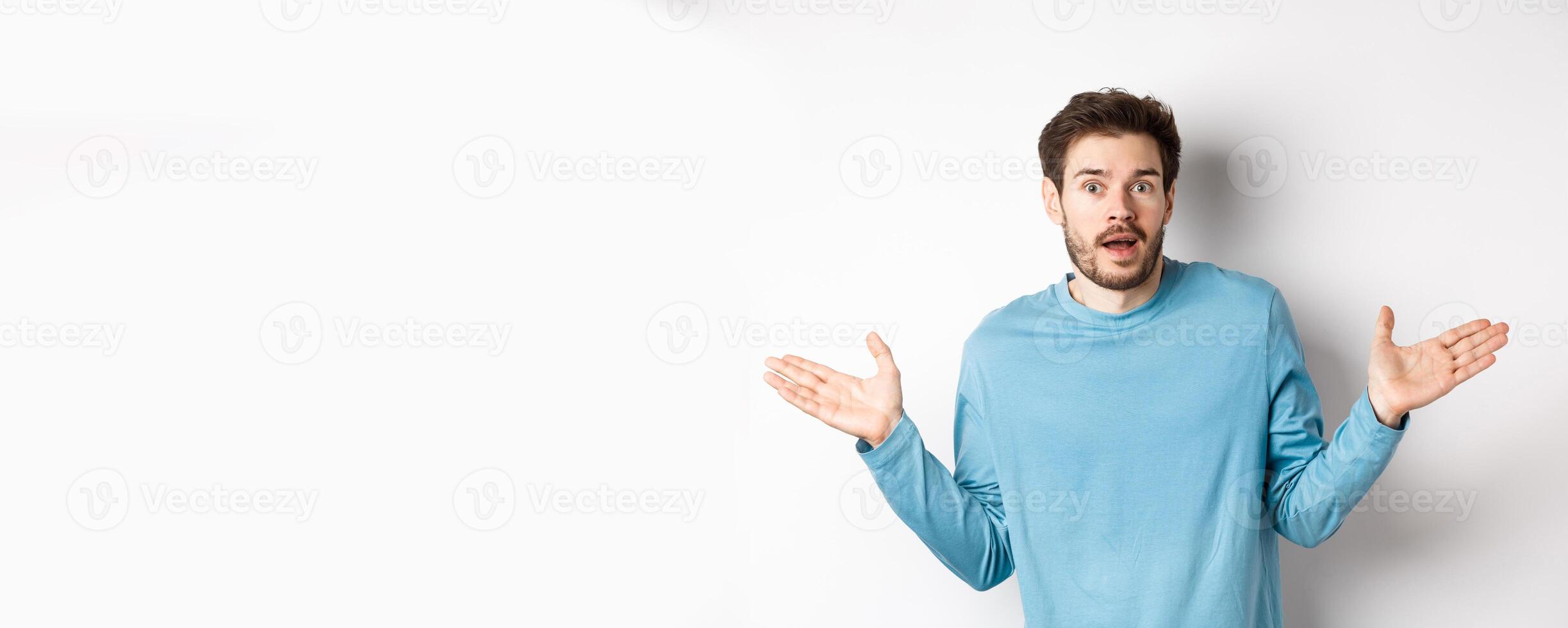 Unbelievable. Amazed young man looking with disbelief, spread hands sideways and staring impressed, standing over white background photo