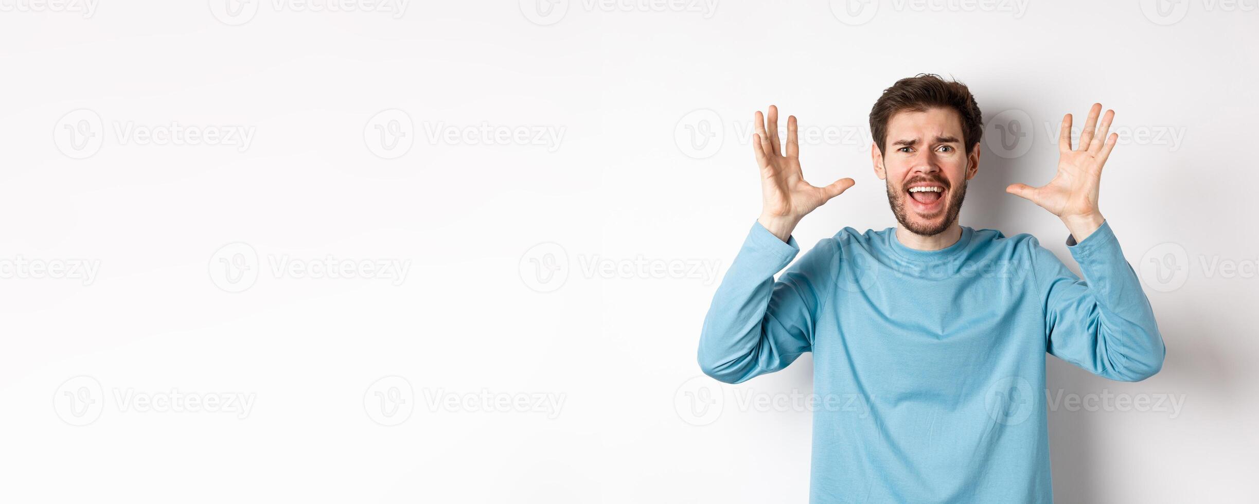 Image of freaked out young man screaming and shaking hands, shouting at camera frustrated or worried, panicking over white background photo