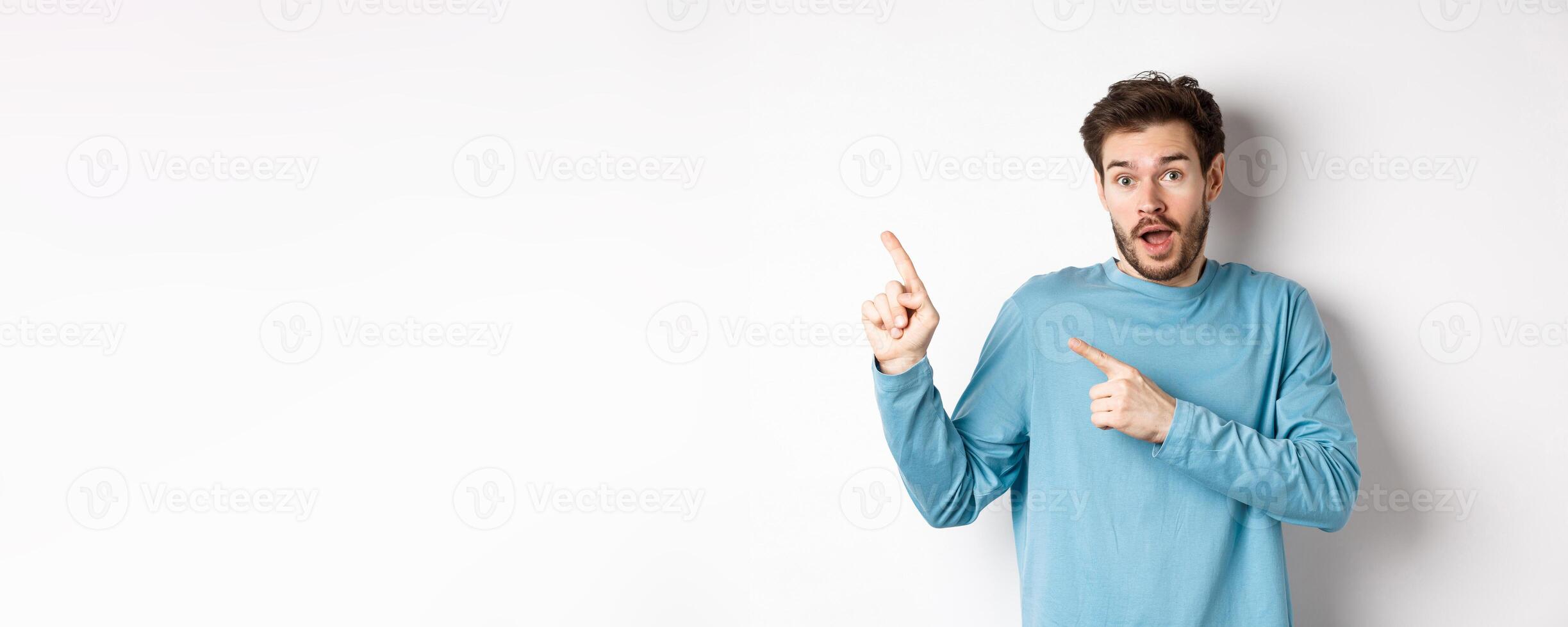 Amazed man showing awesome promo offer, pointing fingers at upper left corner logo and looking excited, recommend product, white background photo