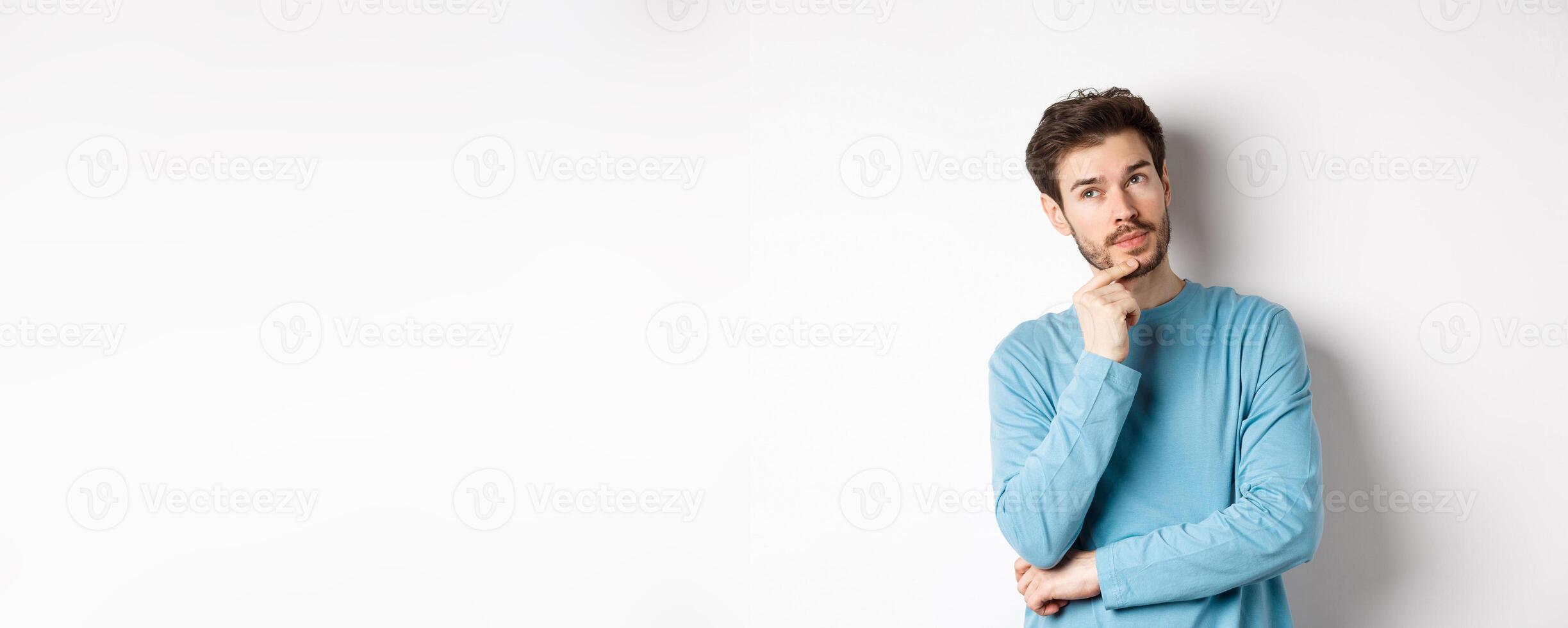 Image of handsome young man making choice, thinking and looking pensive up, standing over white background photo