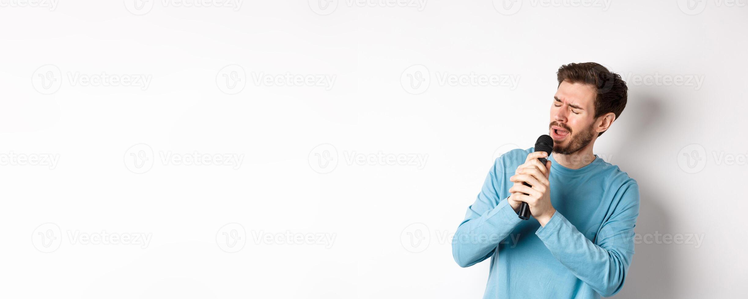 Romantic man singing song in microphone at karaoke, standing over white background photo