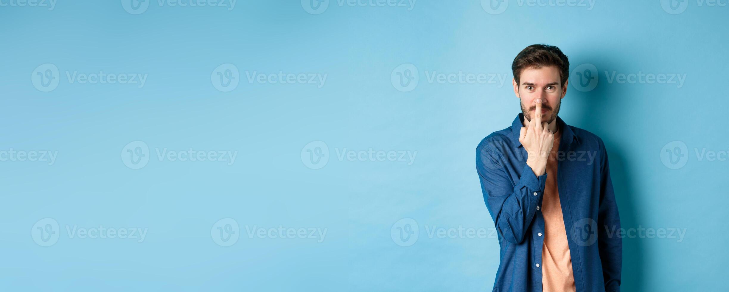 Ignorant and rude guy showing middle finger and smiling, say fuck you, standing on blue background photo