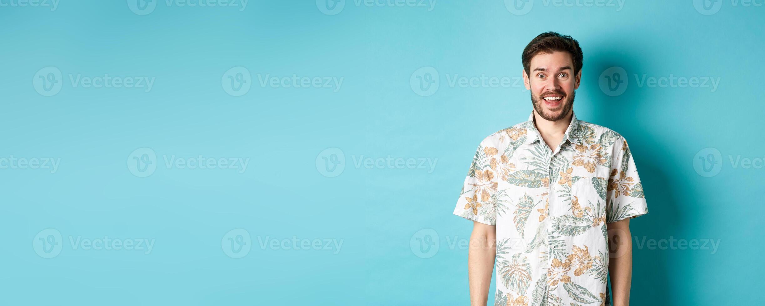 Summer holiday. Handsome happy man in hawaiian shirt looking amused, smiling at camera, standing on blue background photo