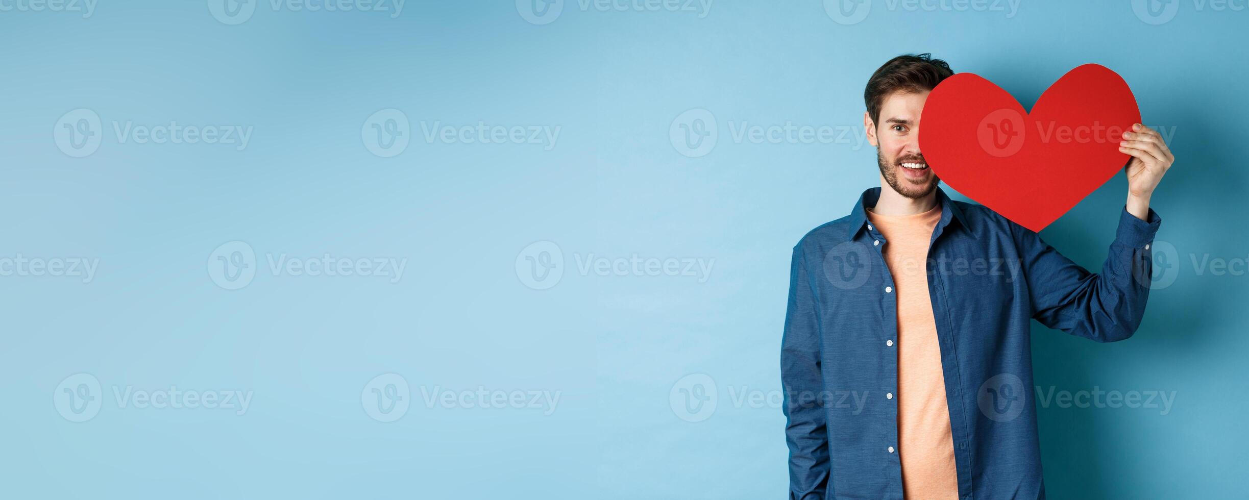 Happy man showing valentines heart and smiling, make romantic gift on lovers day, standing over blue background photo