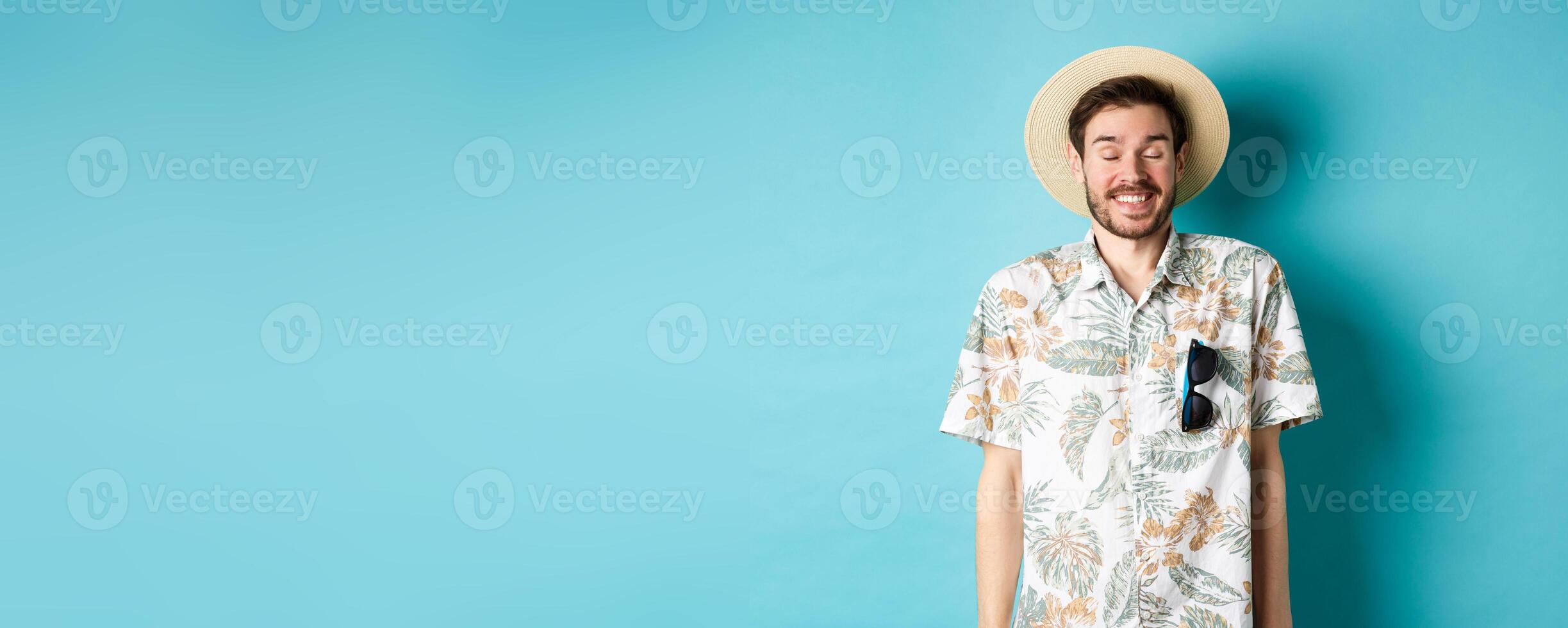 Happy tourist enjoying summer holiday, wearing straw hat and hawaiian shirt, standing joyful on blue background photo