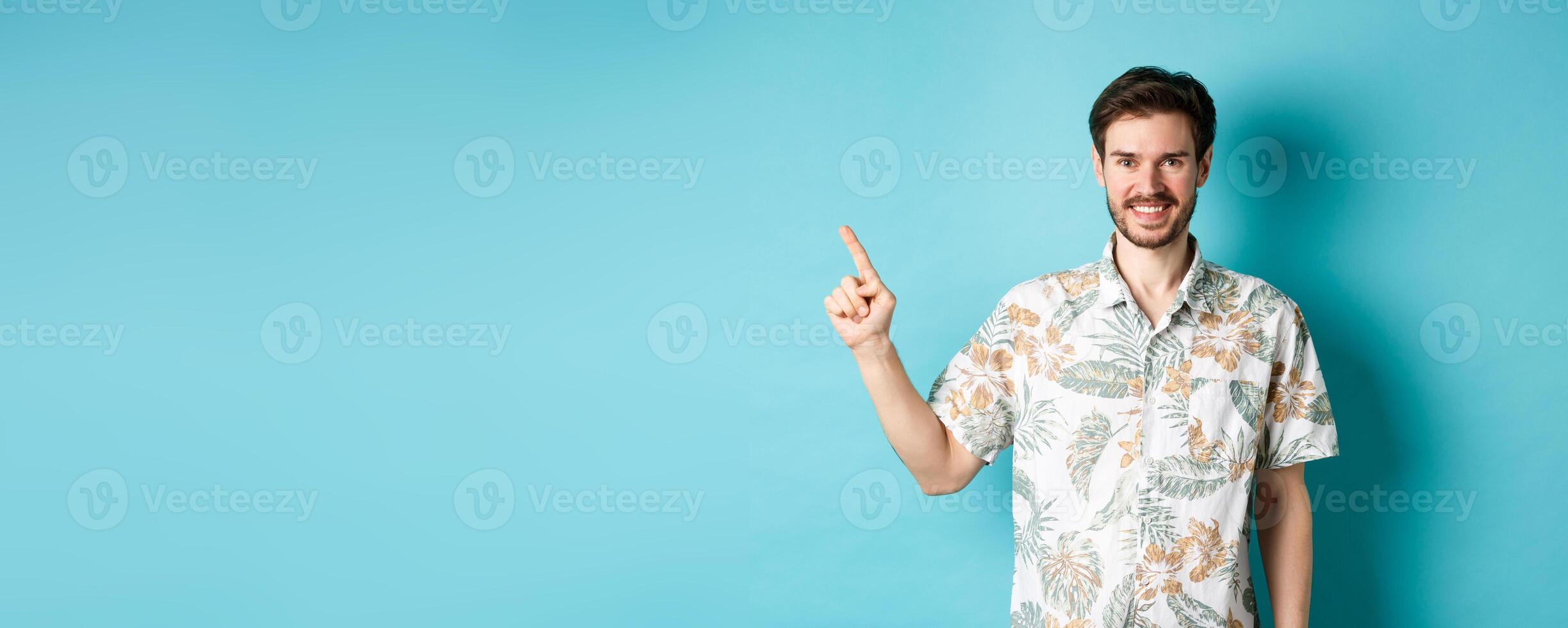 Smiling tourist in hawaiian shirt pointing finger at empty space, showing logo. Concept of vacation and travelling photo