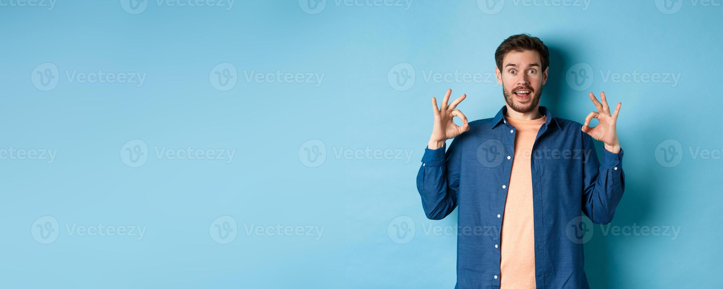 Impressed man praising something awesome, showing okay signs and looking amazed, complimenting good thing, standing on blue background photo