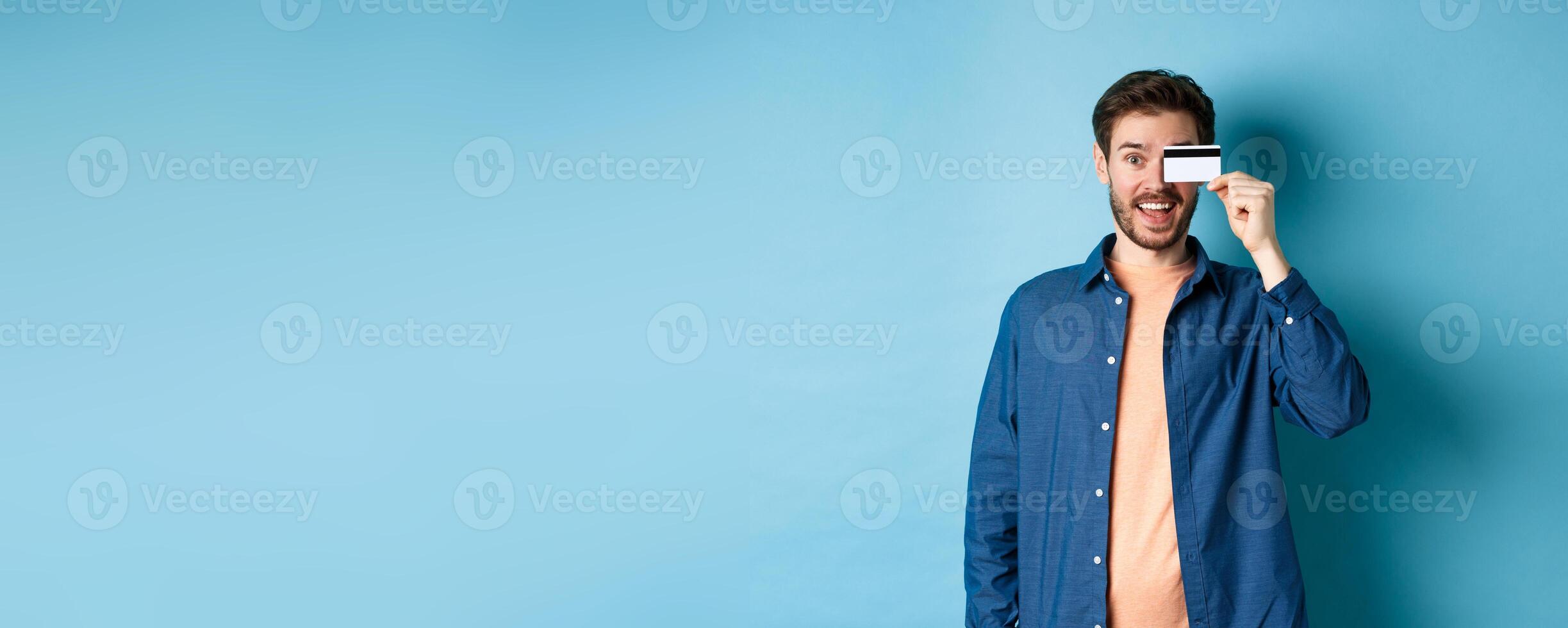 Cheerful handsome man showing plastic credit card and looking excited, checking out special offer, standing on blue background photo
