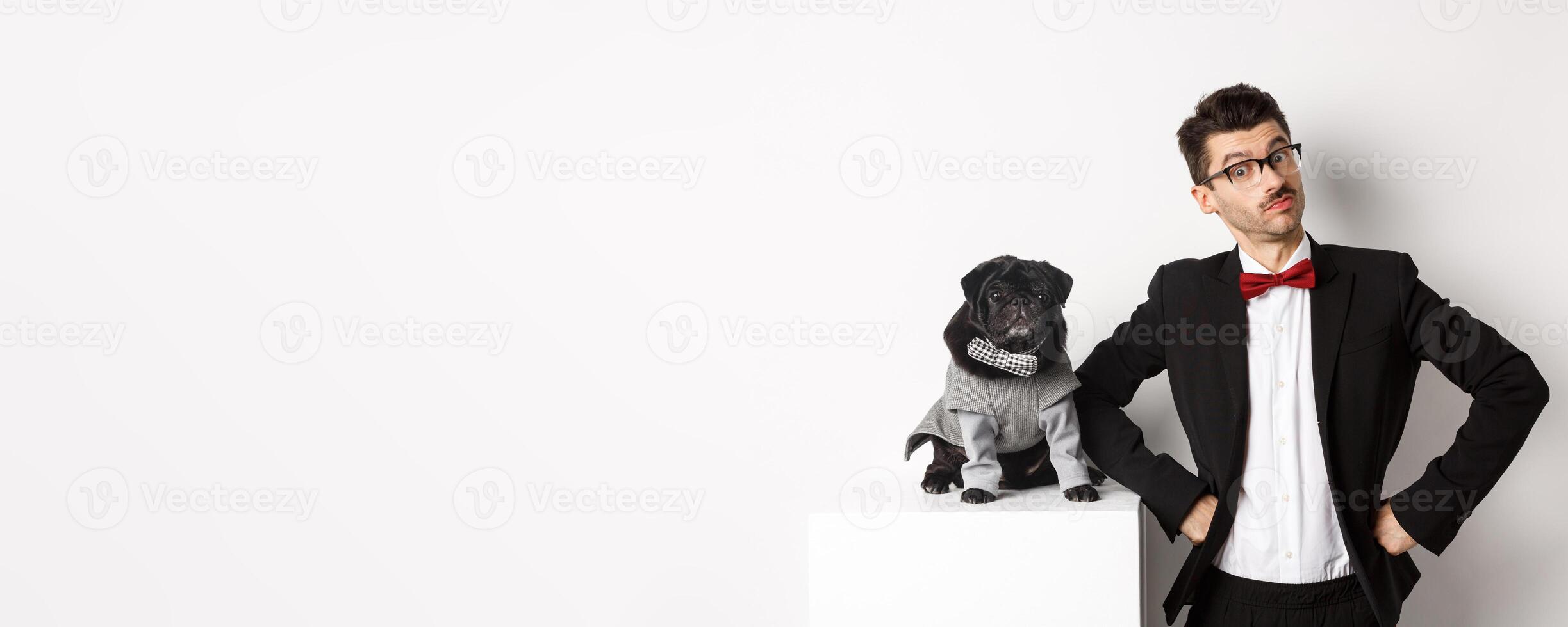 Animals, party and celebration concept. Handsome young man and puppy in formal suits looking at camera, standing over white background photo