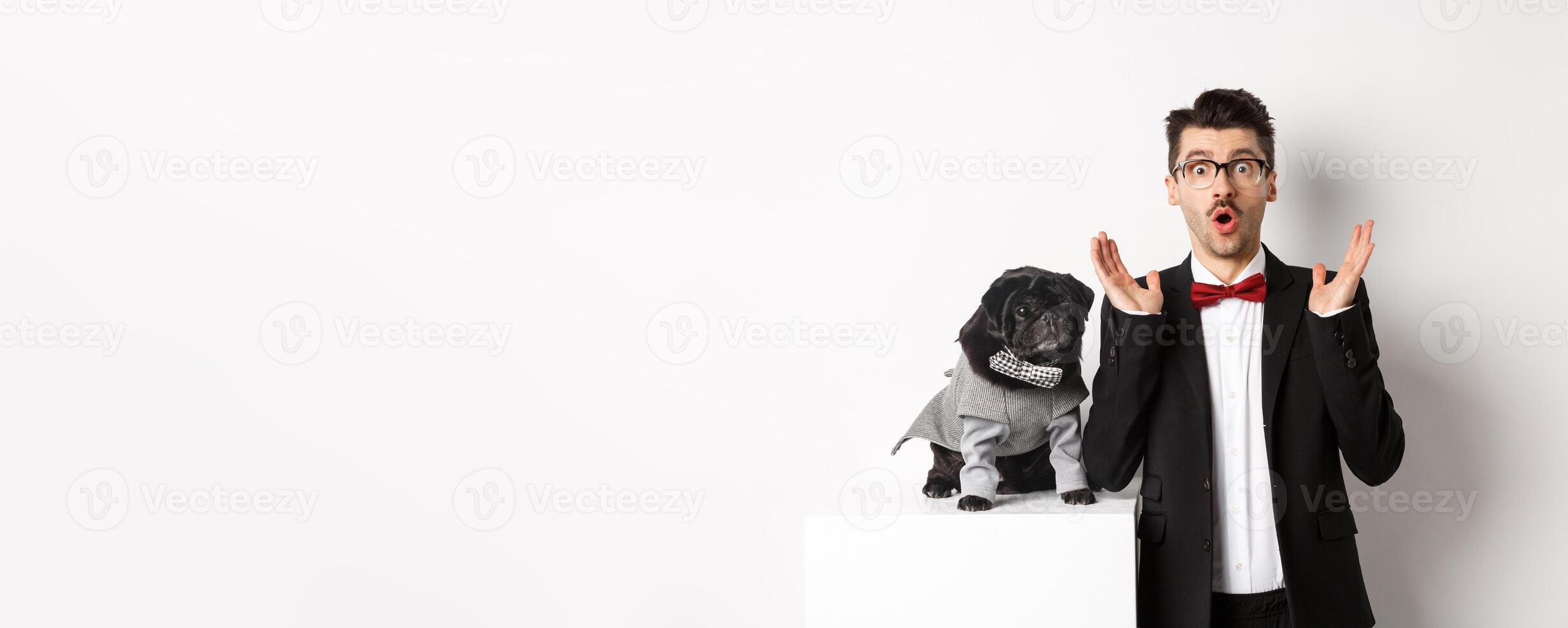 Animals, party and celebration concept. Image of dog owner and cute pug in costumes suits staring surprised at camera, reacting on promo offer, white background photo