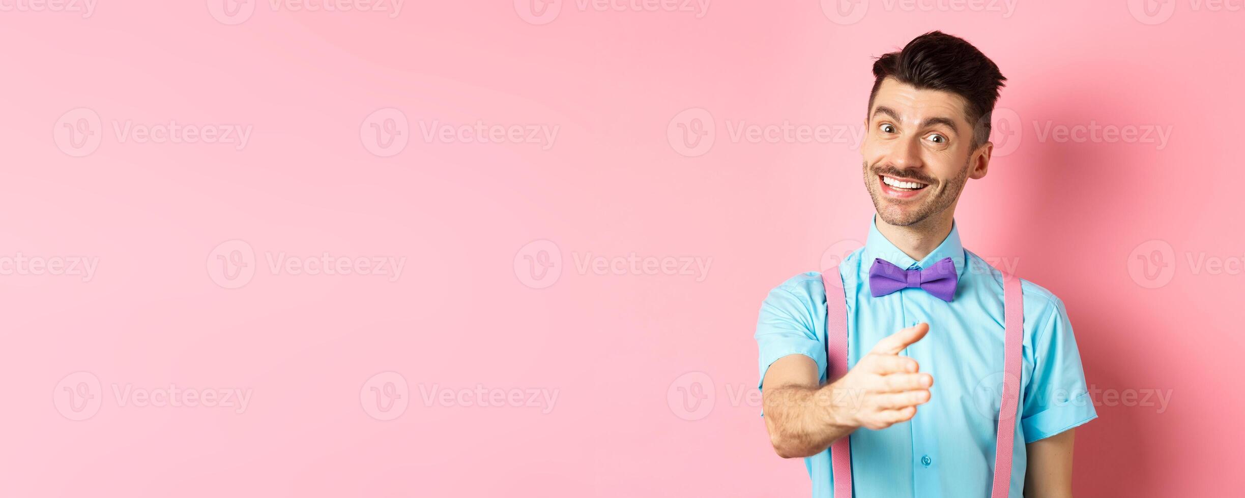 Nice to meet you. Handsome young man stretch out hand for handshake, smiling friendly and polite, introduce himself, standing over pink background photo