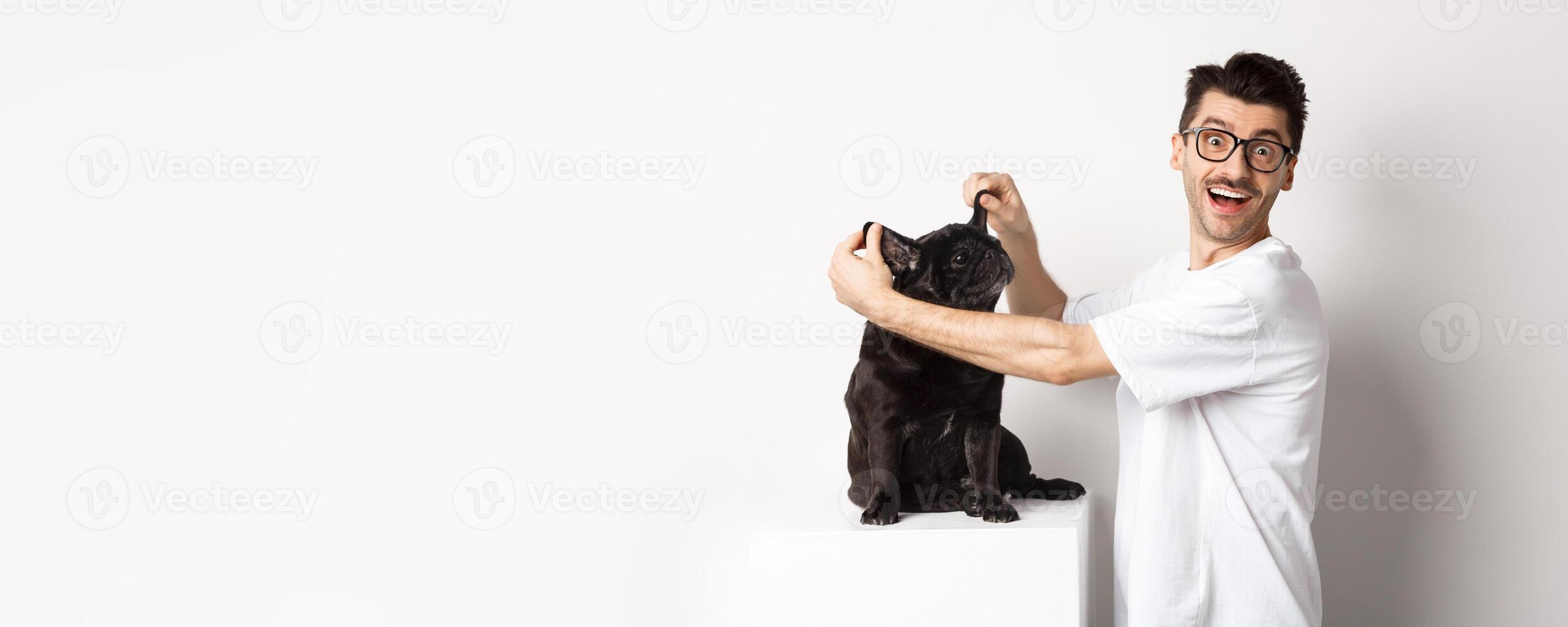 Happy young man looking at camera, showing cute dog ears and feeling rejoice, adopting a pet, standing over white background photo
