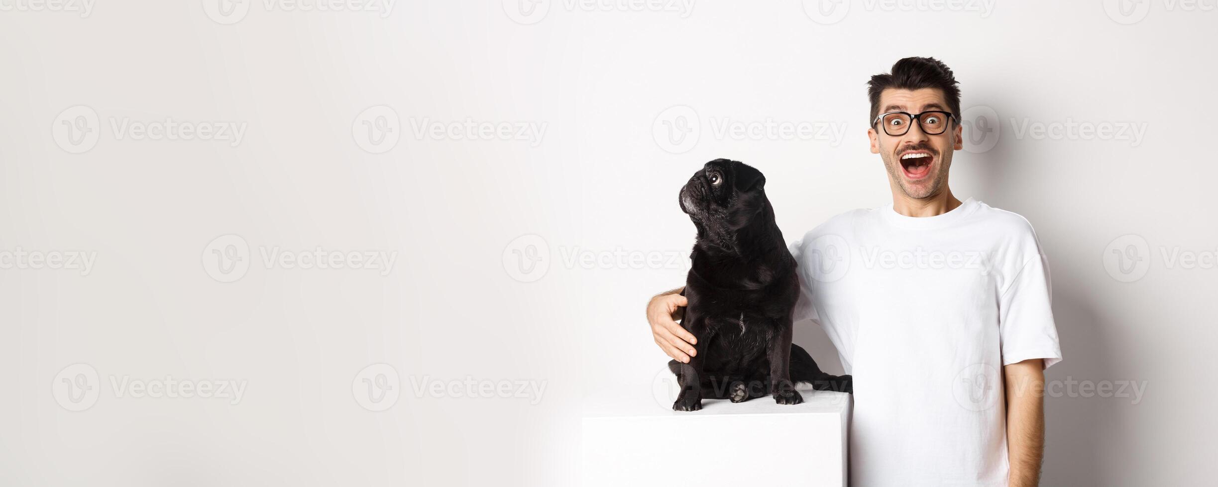 Image of amazed man staring at camera while his small dog looking left at copy space, standing over white background photo