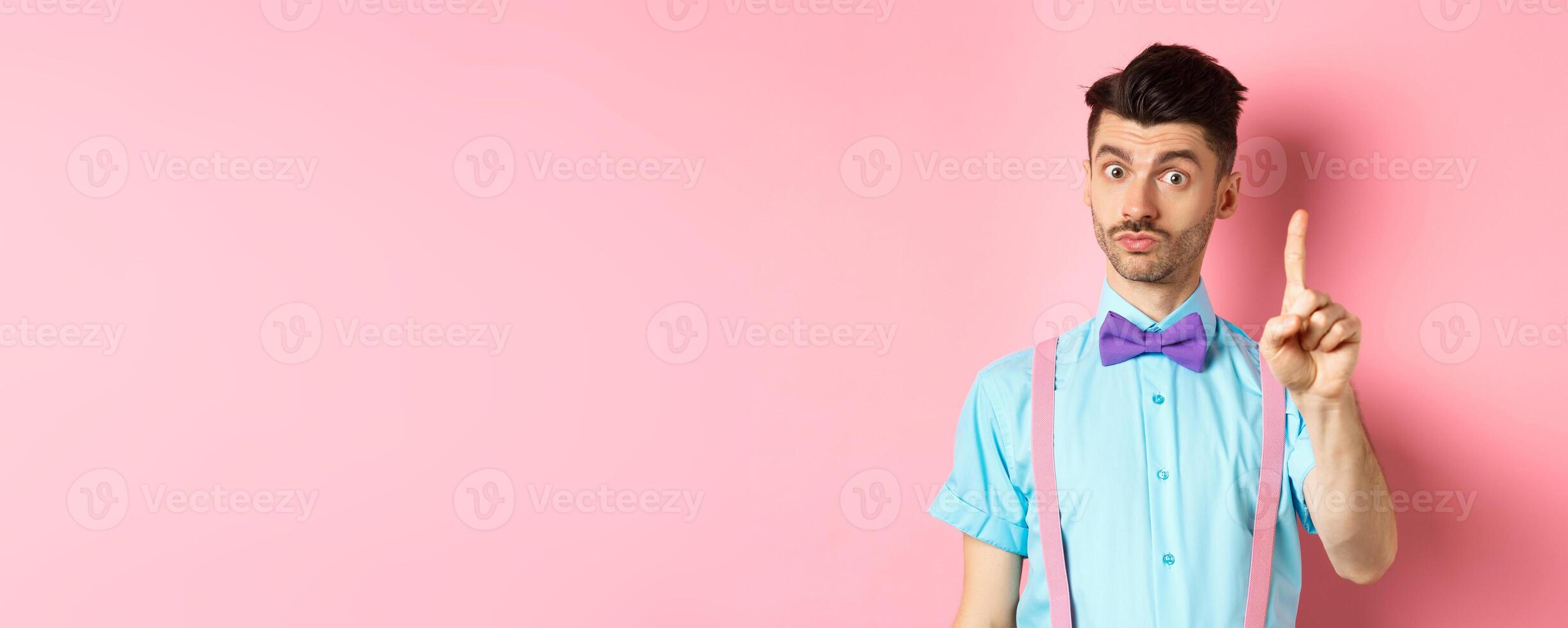 Young funny guy showing finger to explain something, prohibit or warn you, standing on pink background photo
