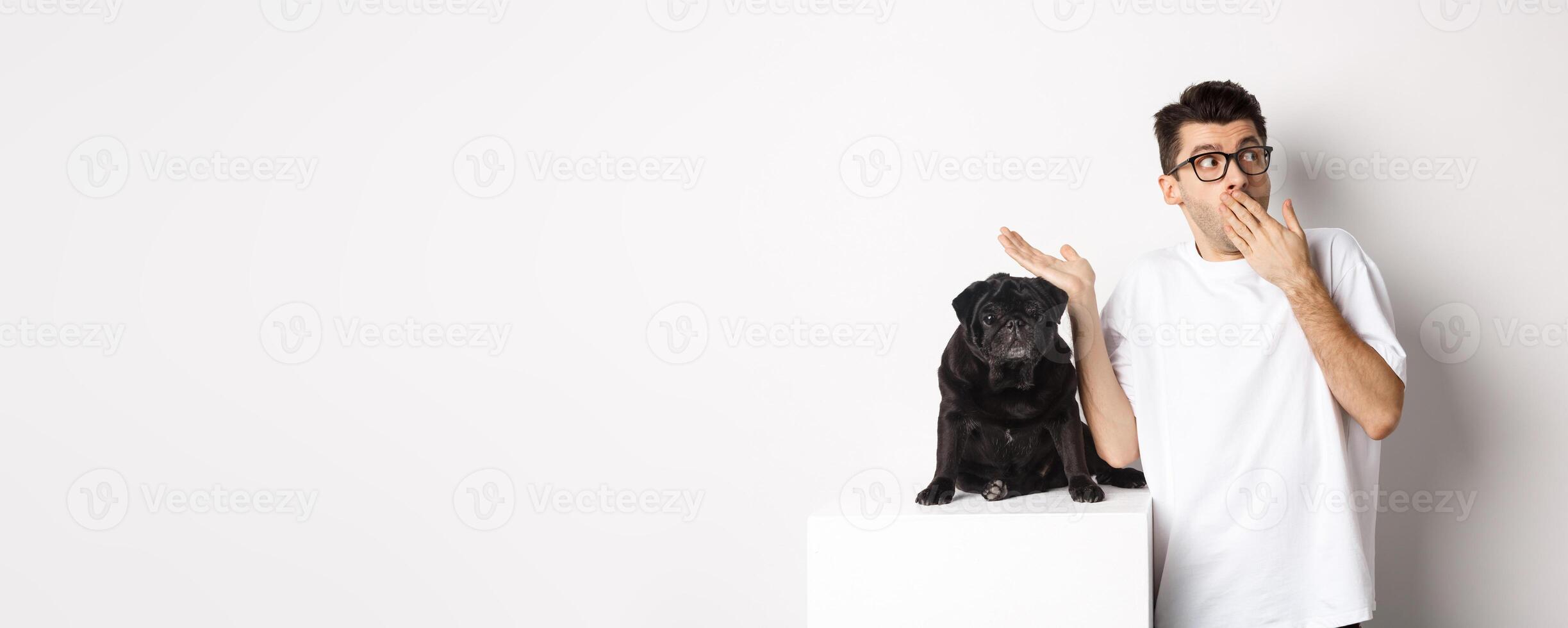 Surprised and shocked man in glasses, standing near cute black dog and staring right at logo, posing over white background photo