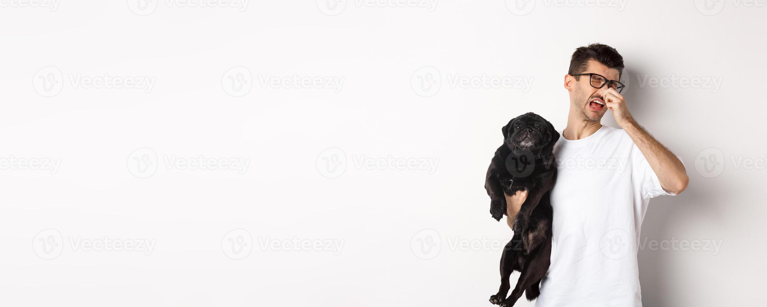 Dog owner squinting and shutting nose from disgusting reek, holding pug with bed smell, standing over white background photo