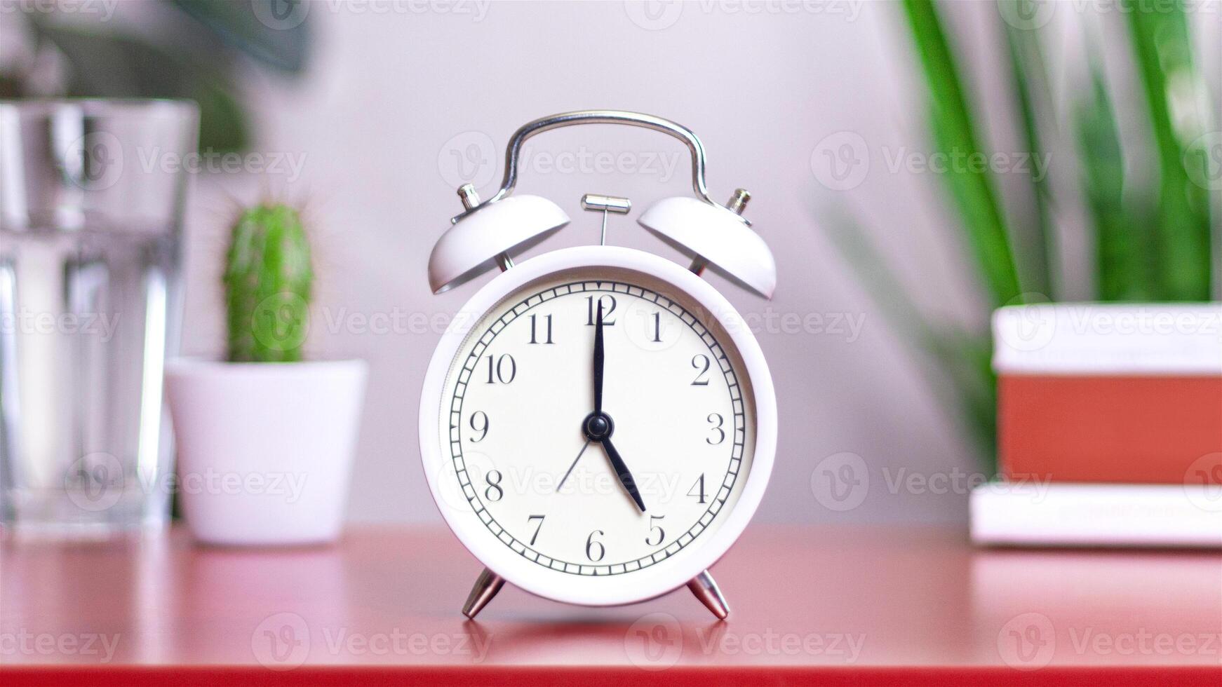 Classic white clock on a table. The clock hand points to 5 or 17, close up photo