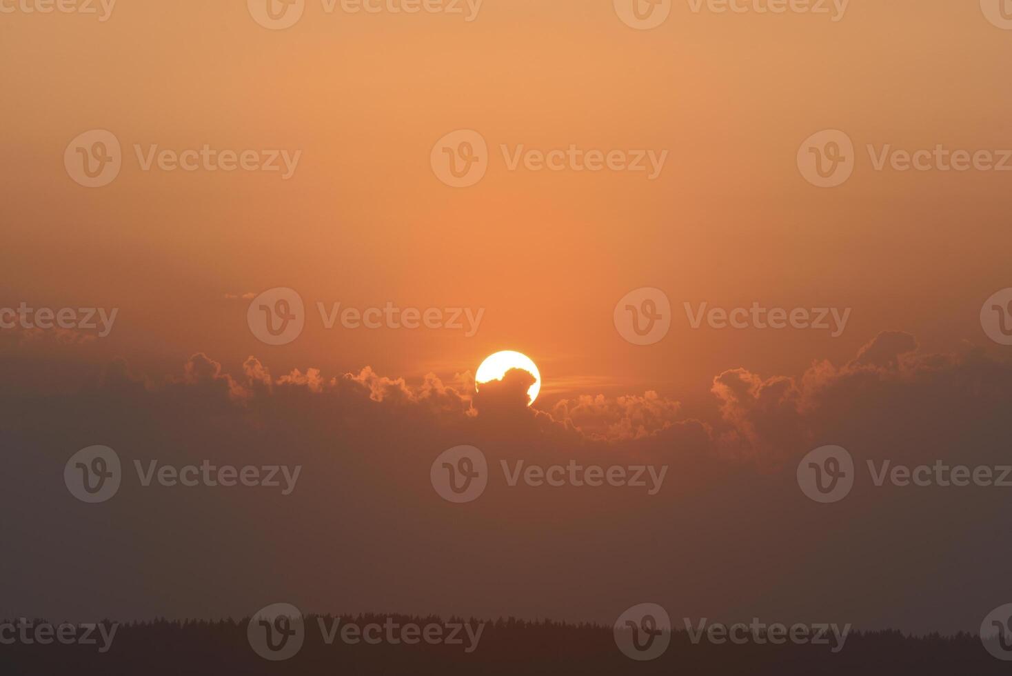 The solar disk. The setting sun in a cloud over the forest. photo