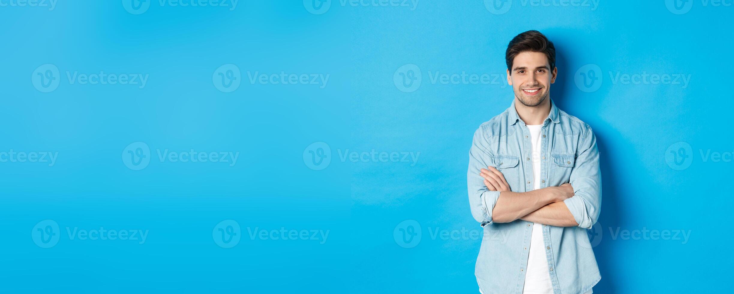 Handsome guy in casual clothes standing with arms crossed and confident smile against blue background photo