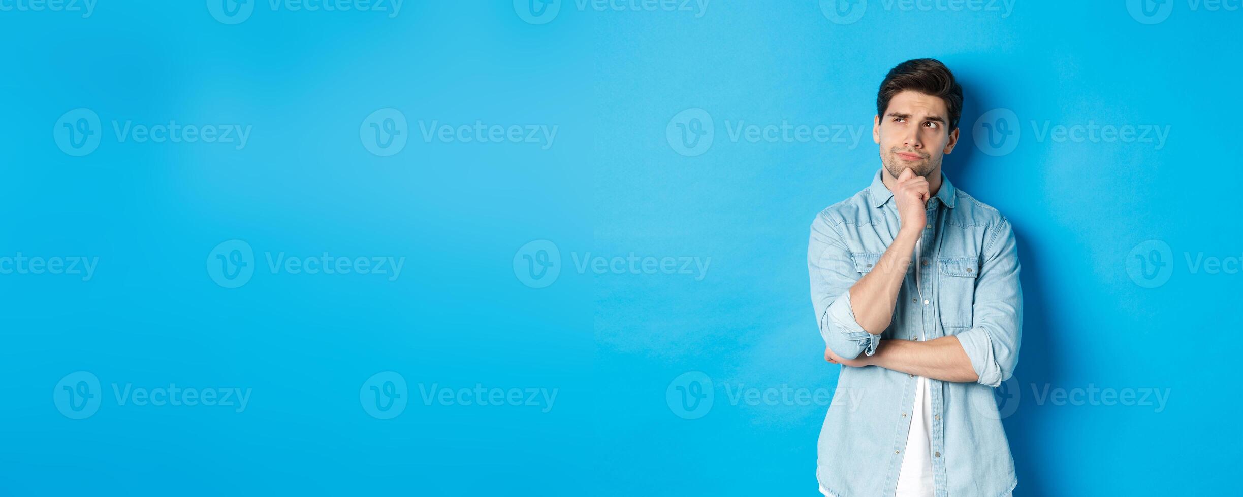 Image of adult bearded man 25s years, thinking about something, looking at upper left corner and pondering ideas, standing over blue background photo