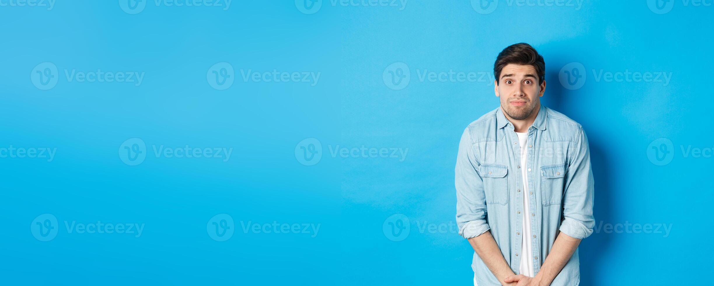 Embarrassed guy want to pee, waiting in line for toilet, standing against blue background photo