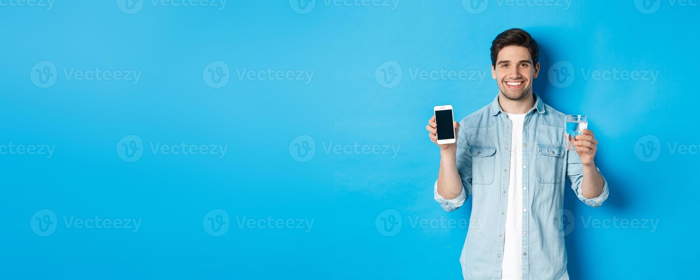 Young man control water balance with smartphone app, showing mobile screen app and smiling, standing over blue background photo