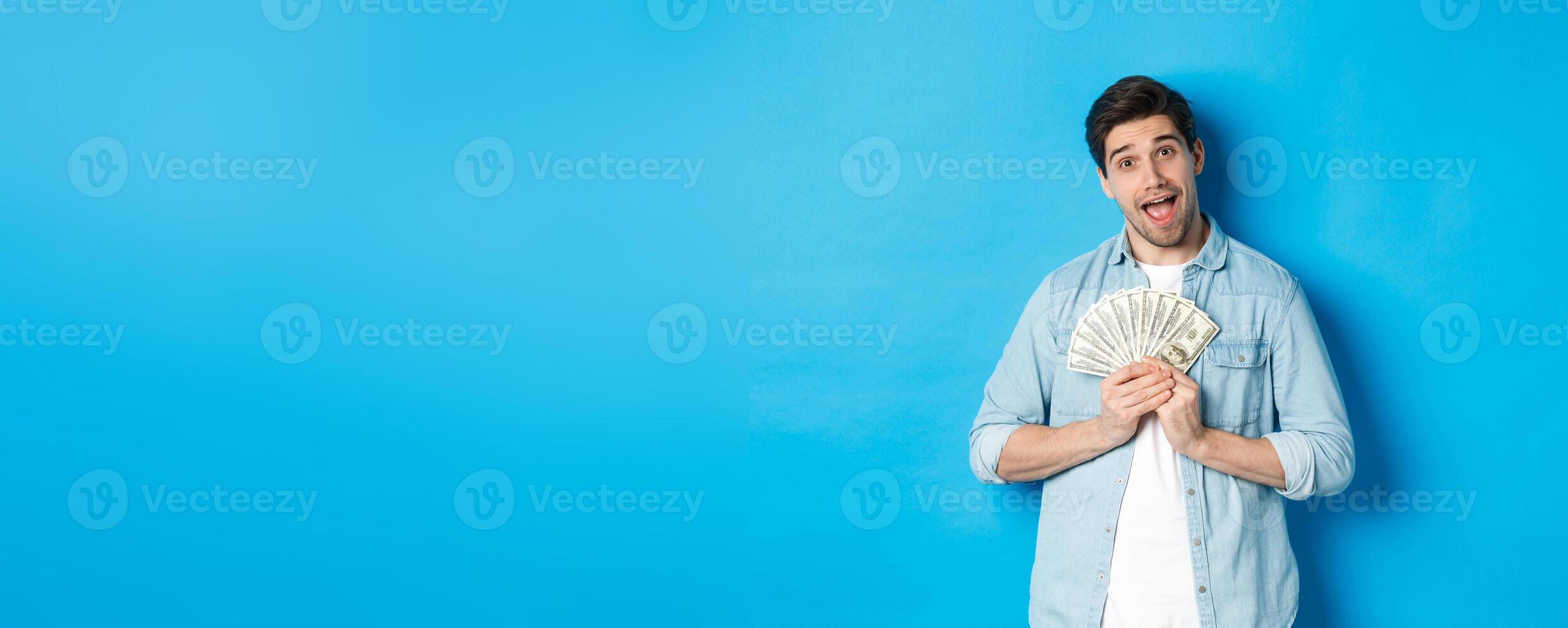 Smiling greedy guy hugging money and smiling, unwilling to share, standing over blue background photo