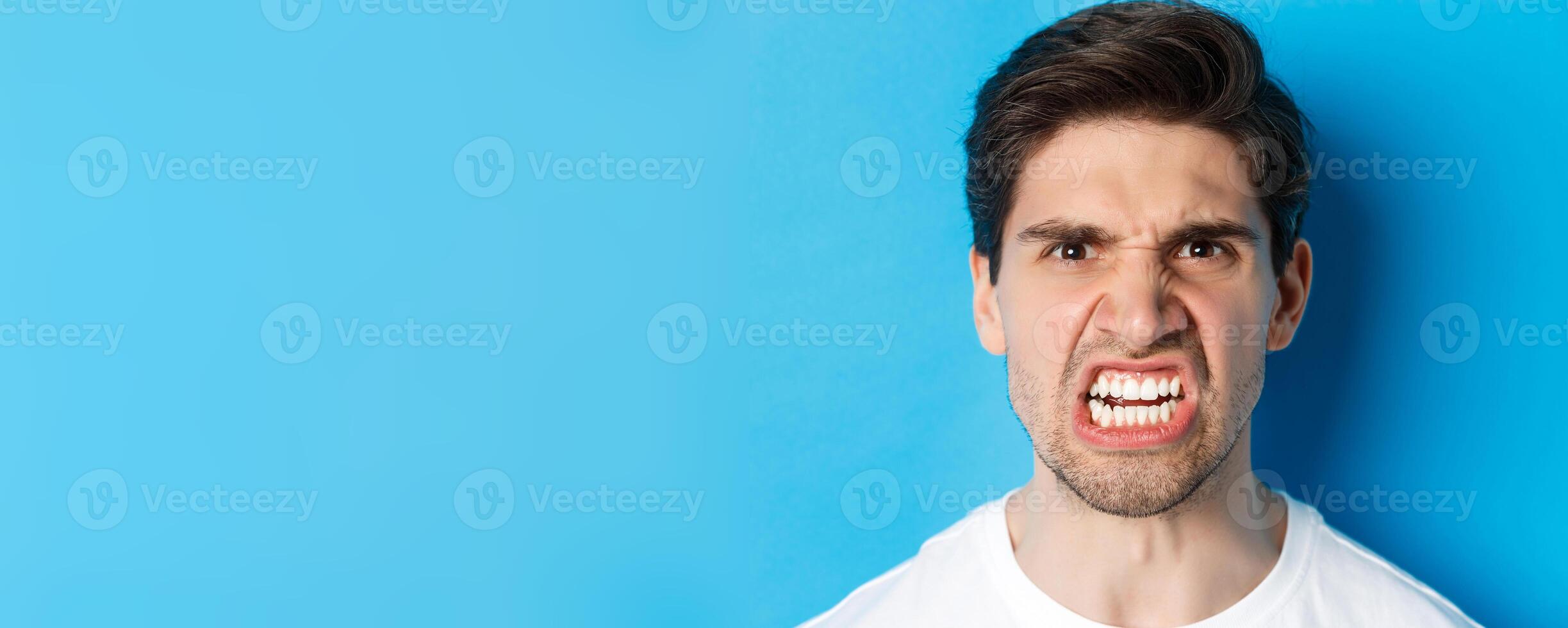 Headshot of angry caucasian man looking with scorn and dismay, being mad at person, standing against blue background photo